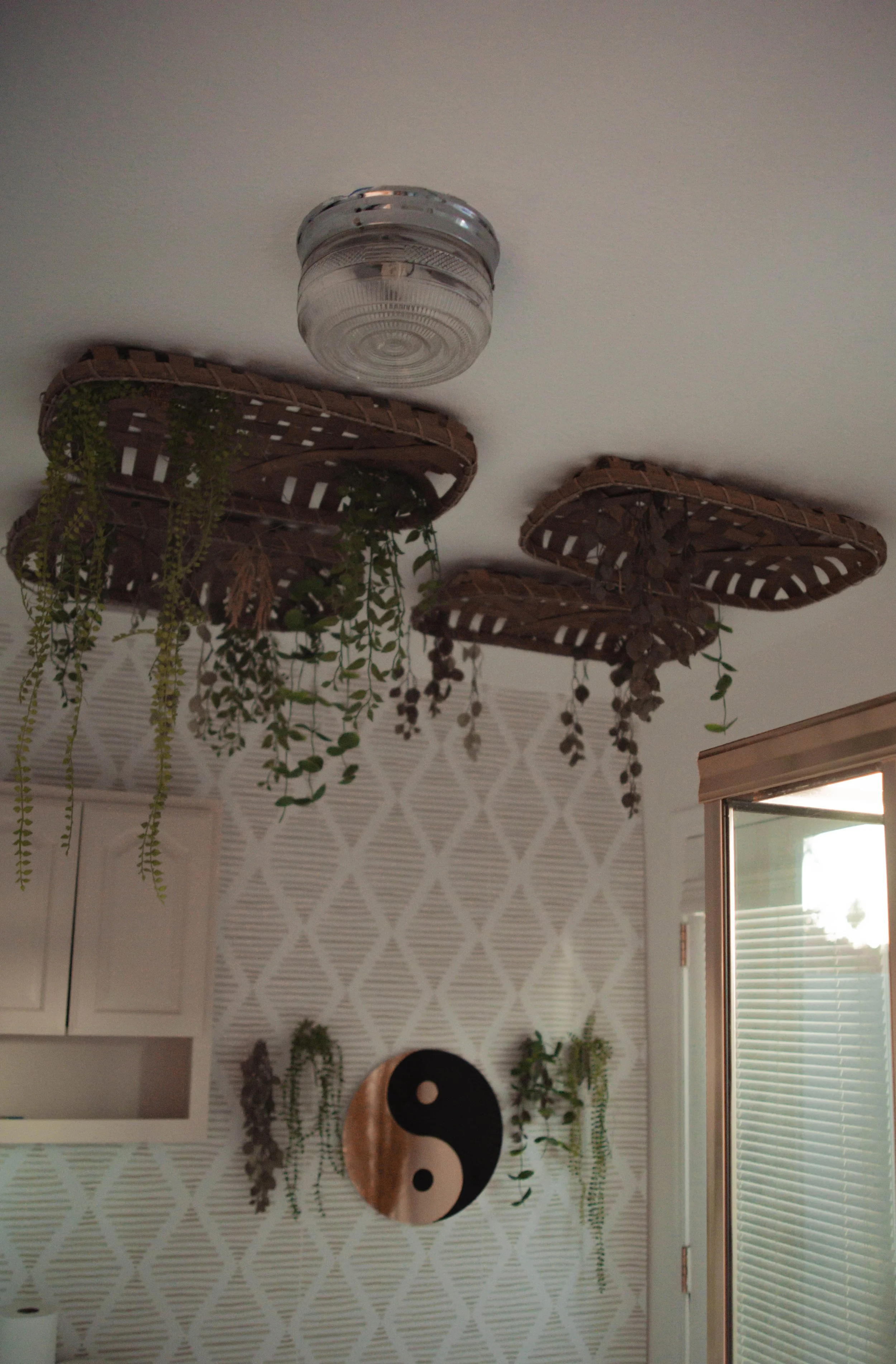 Ceiling-mounted wicker planters with hanging green plants in a room with patterned wallpaper and a yin-yang wall decoration.