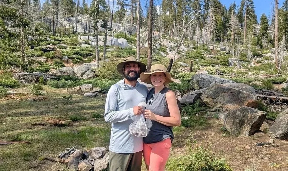 Smiling couple in the woods holding their morel mushroom finds from a Sierra Nevada foraging tou