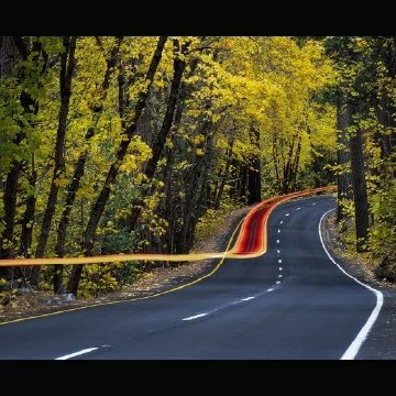 A creative composition with two pictures of winding road through a forest with autumn-colored trees and streaks of light from a passing vehicle.