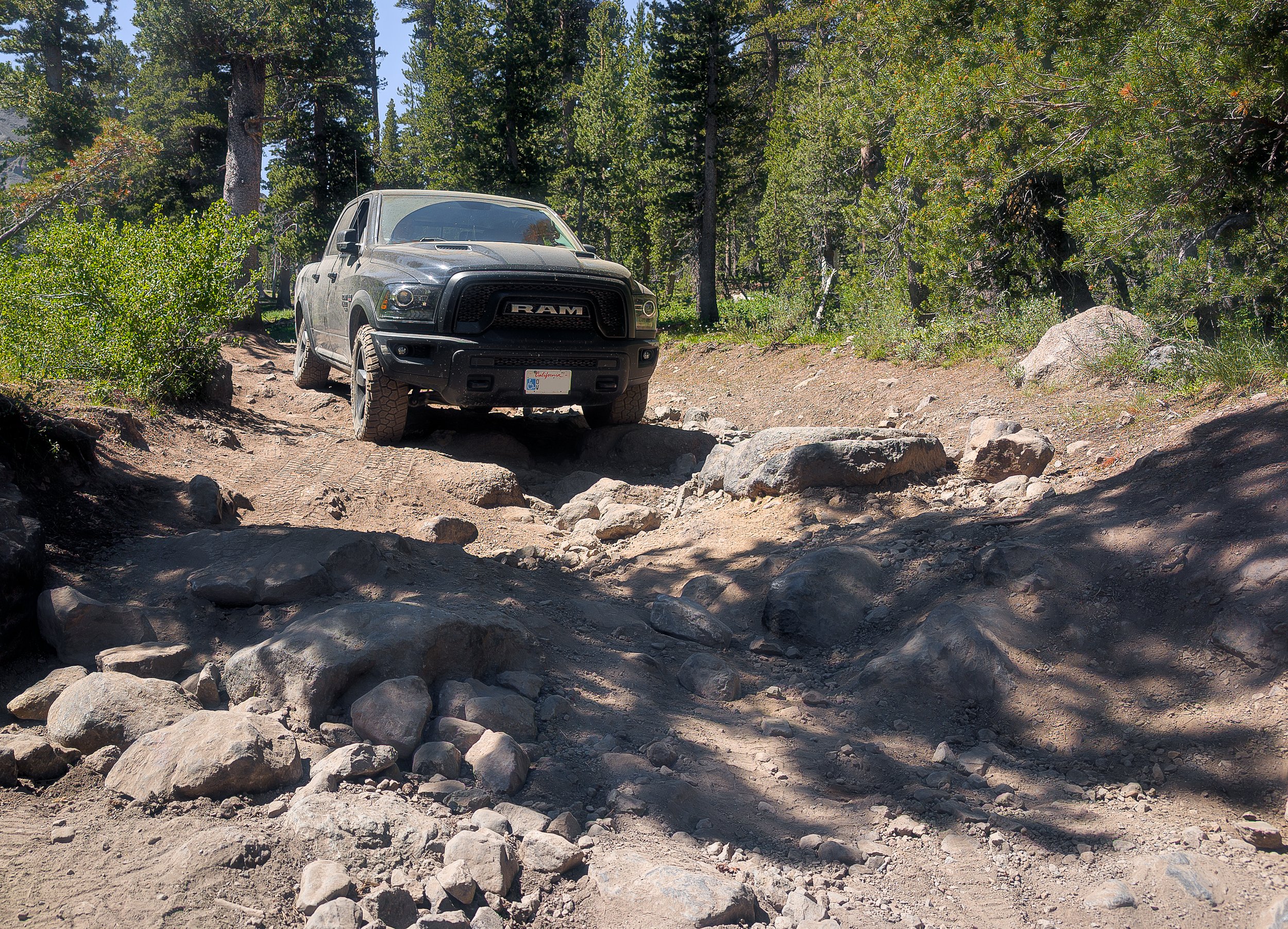 Off-road vehicle descending a rocky forest road in the Sierra Nevada, illustrating terrain assessment and tire placement.