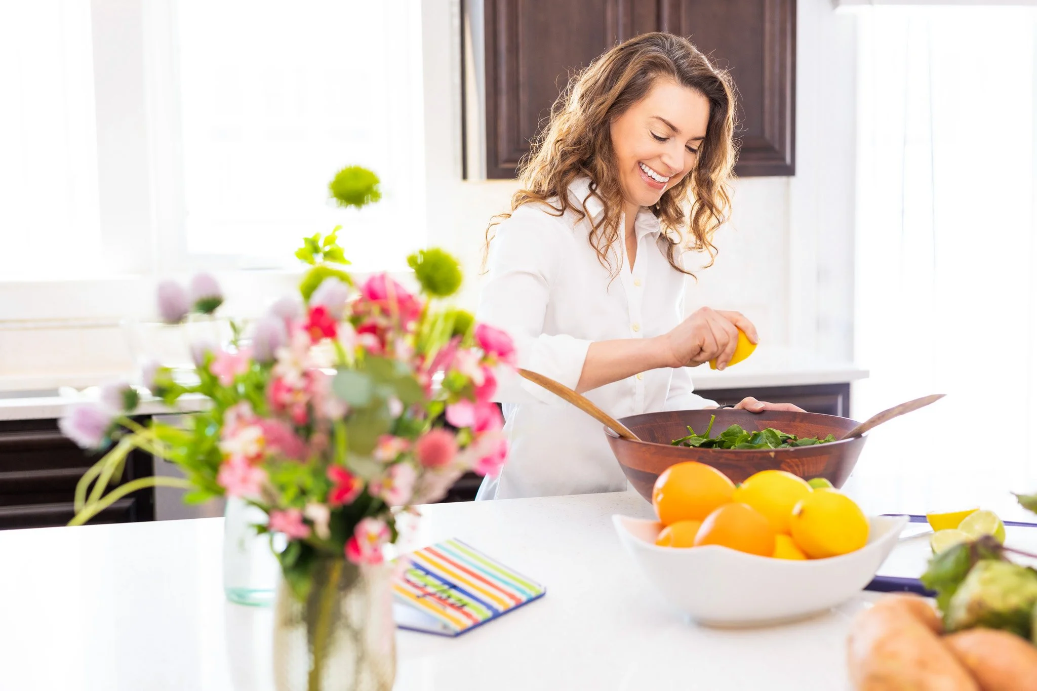 happy smiling personal wellness coach squeezing a lemon on a kitchen island over a bowl of greens