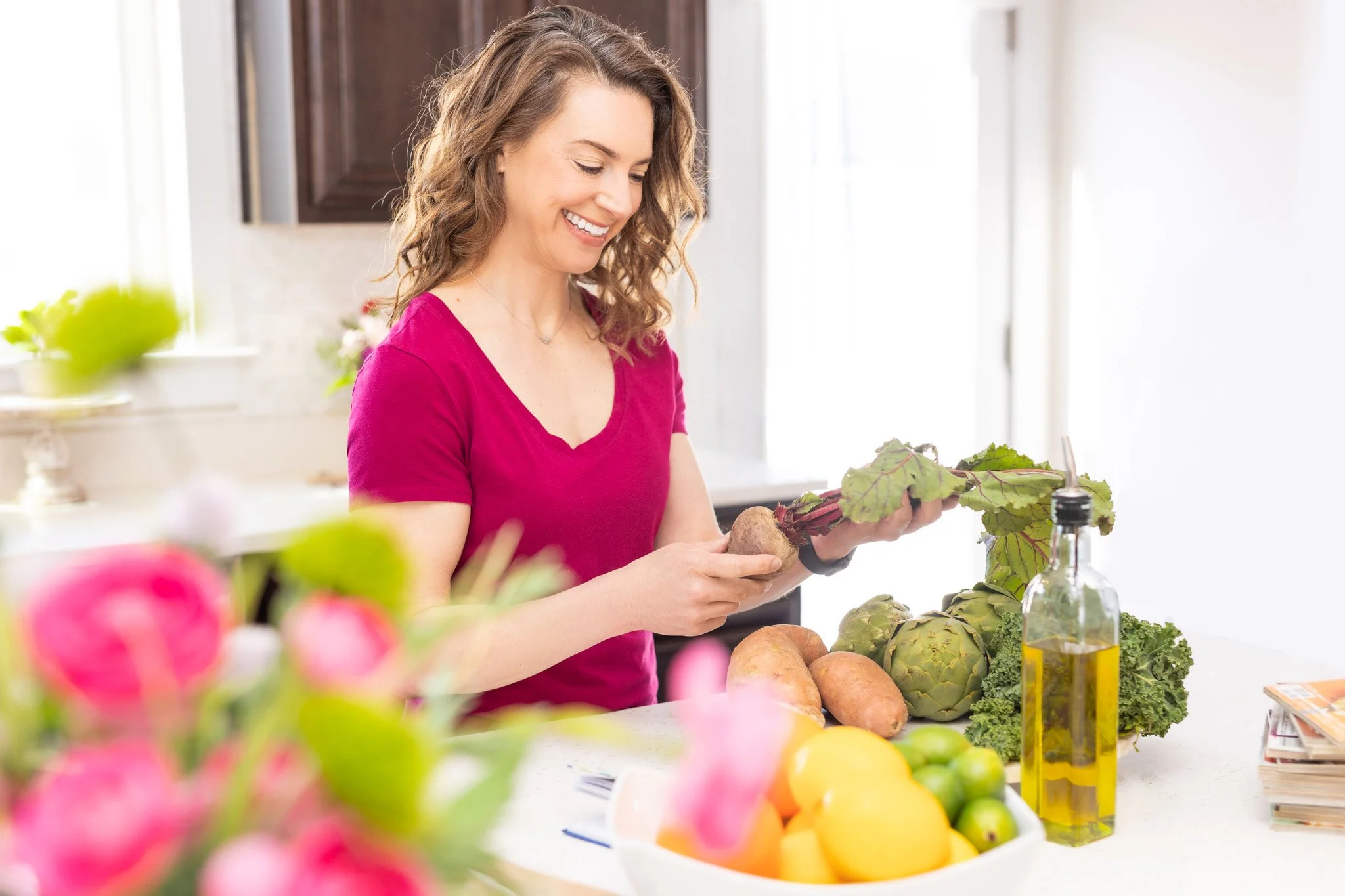 happy smiling personal wellness coach holding beets with flowers and vegetables on the counter