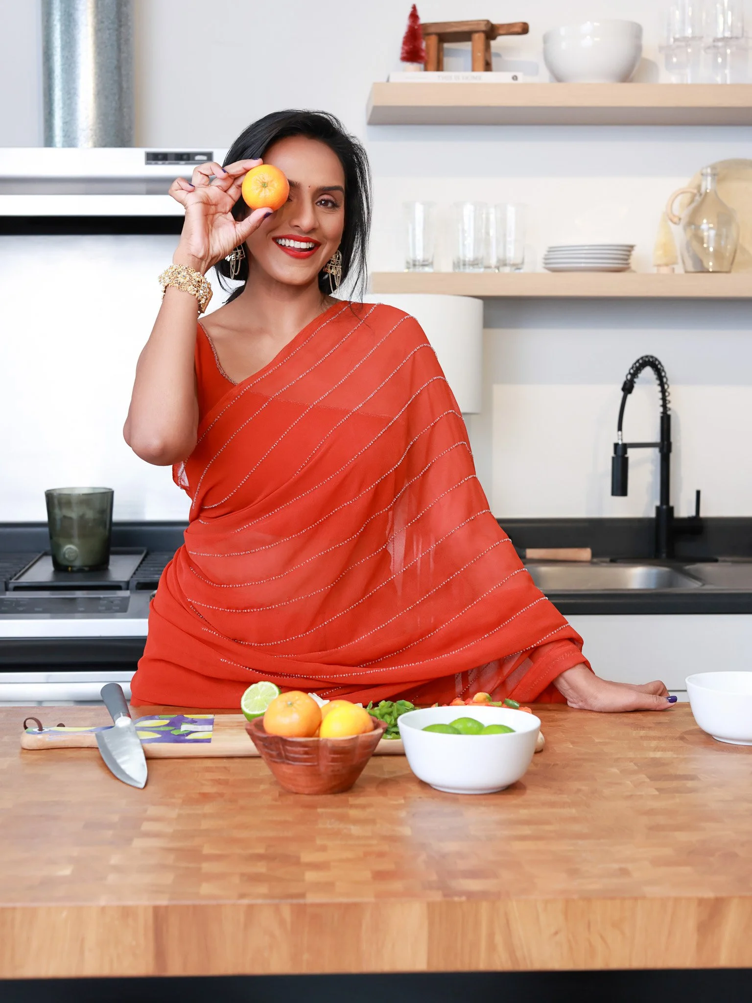 happy smiling Indian woman in a sari cooking and holding an orange up in front of her eye