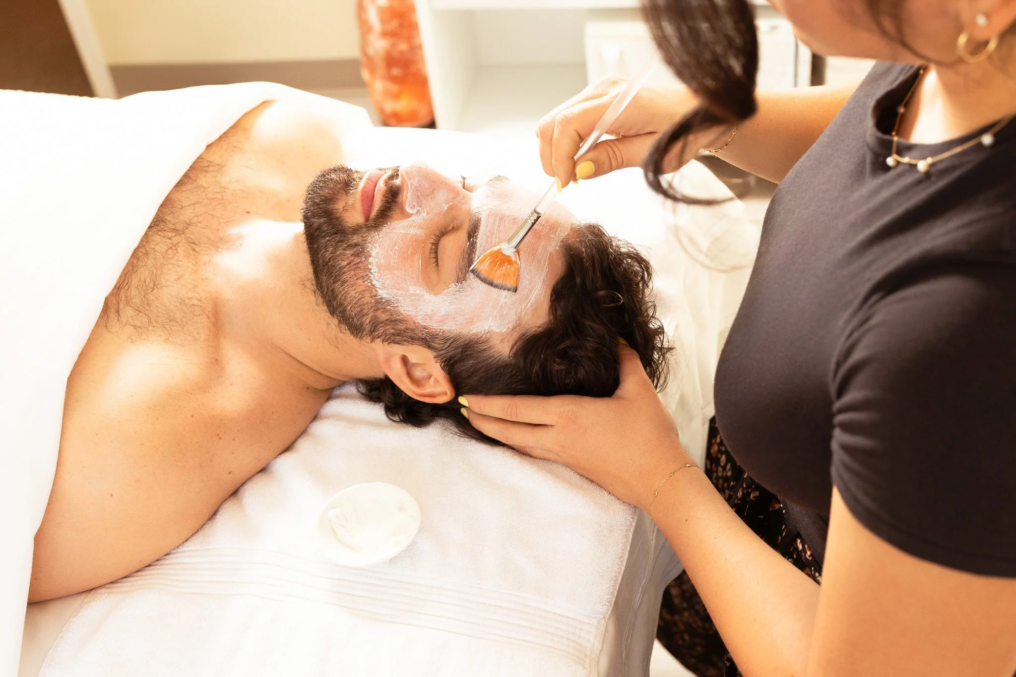 man lying on a spa table receiving a facial from a woman