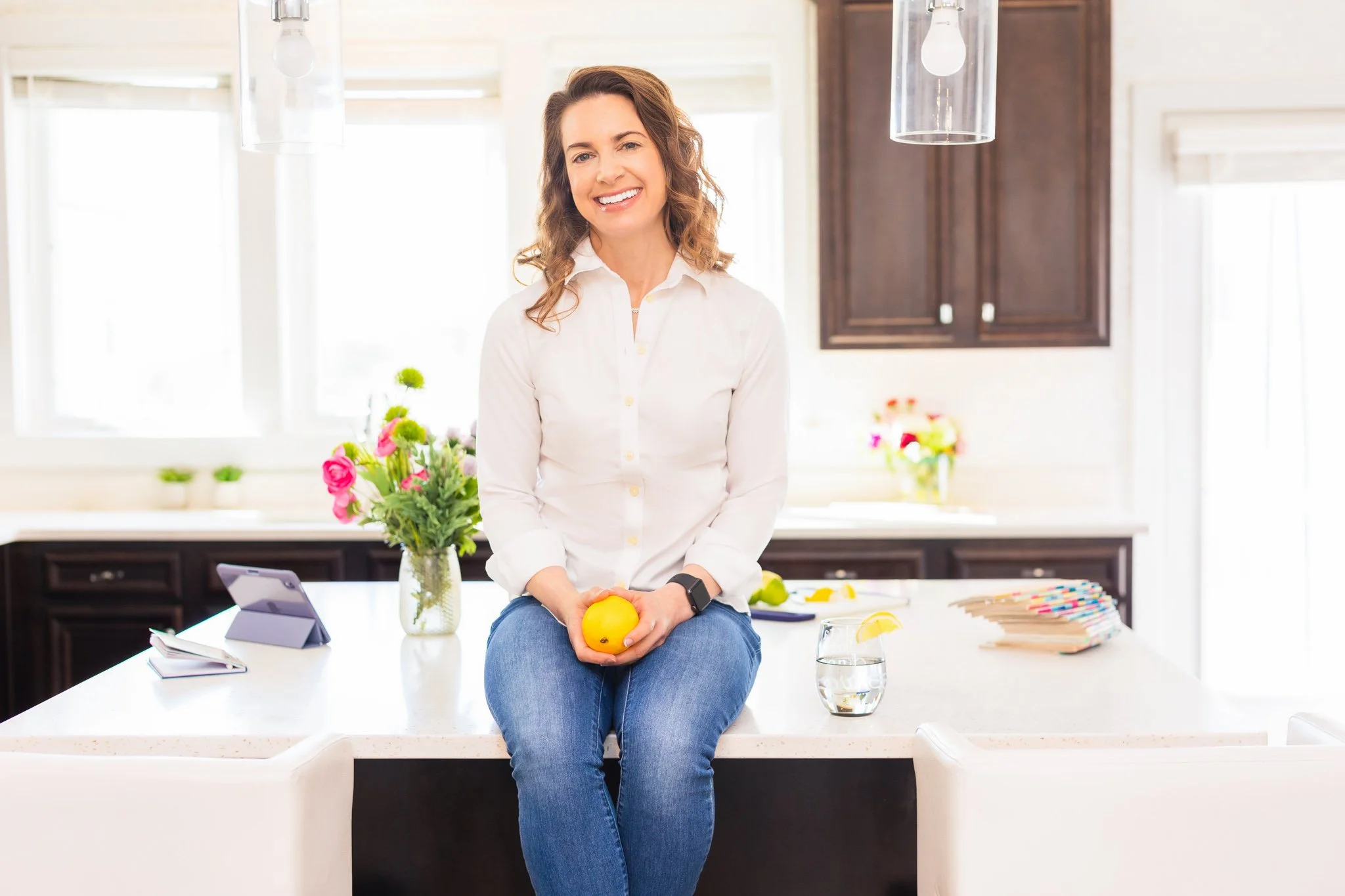 happy smiling woman sitting on a kitchen island holding a lemon