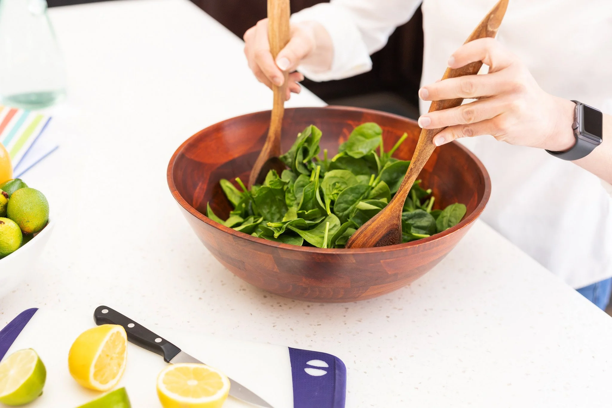beautiful vibrant bowl of greens with a woman's hands tossing the salad