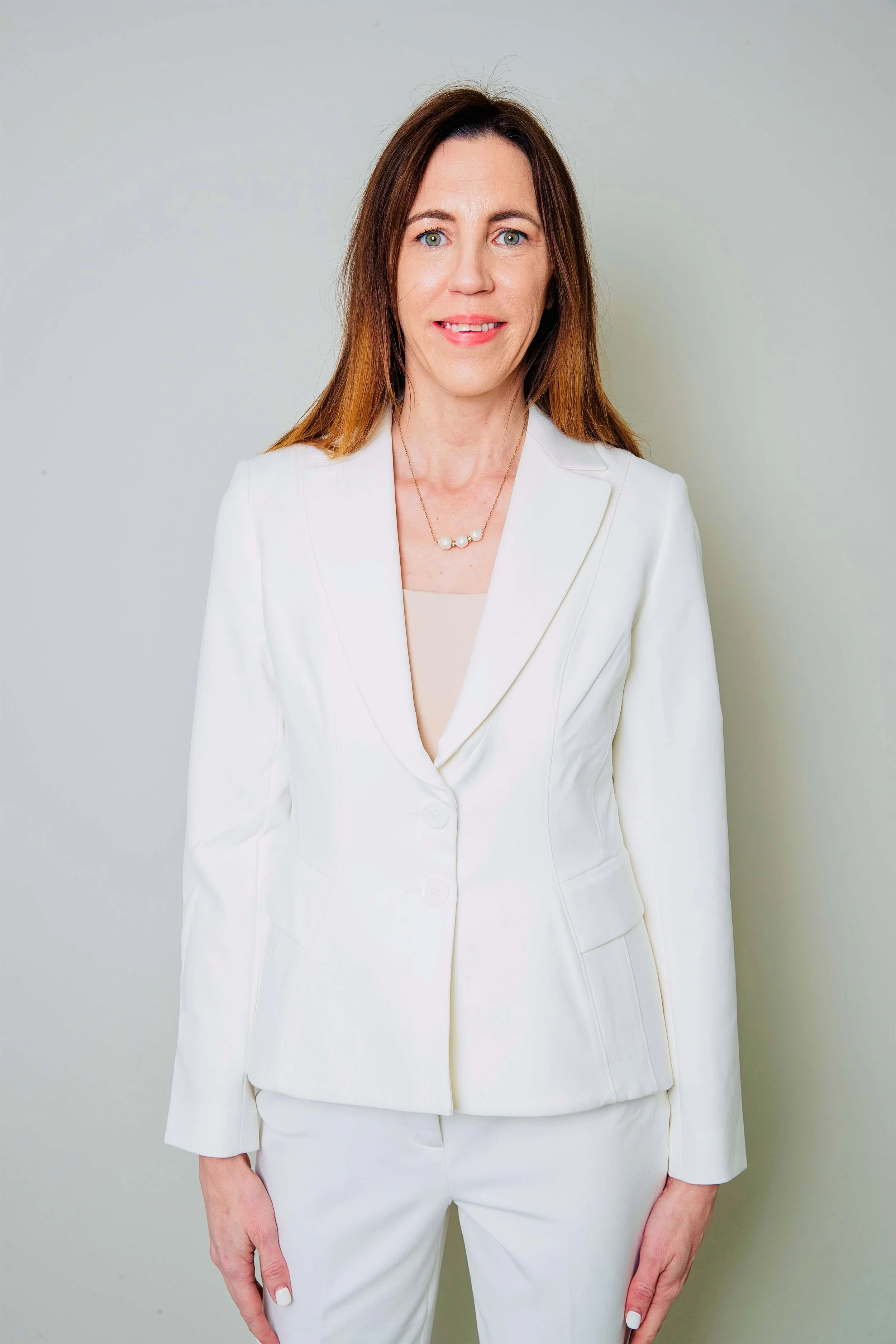 A woman in a white suit with a beige top, standing against a plain light-colored background.