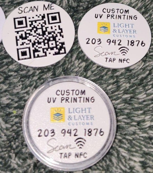 Closer-up of small circular nfc tokens printed with a raised texture that reads 'Custom UV Printing Light & Layer', a phone number, and a QR code.