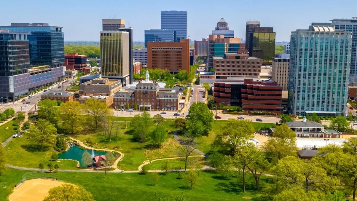 Low overhead image of Clayton, MO featuring several tall buildings of varying designs, with a park in the foreground including walking paths and a small pond.