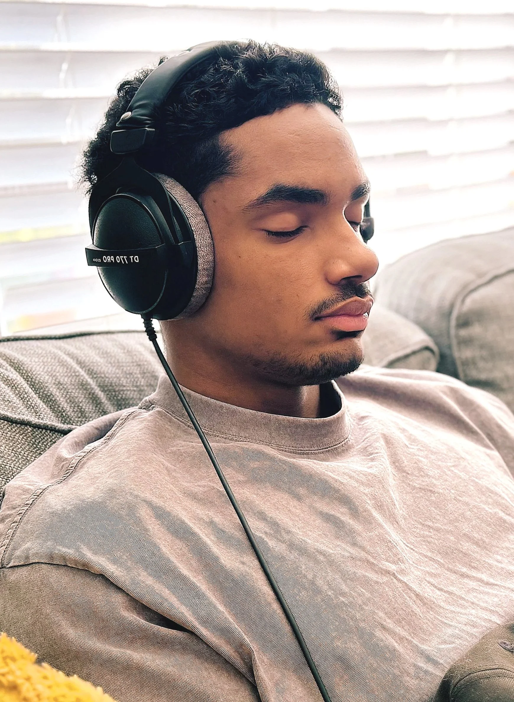 A young man relaxing on a couch wearing large over-ear headphones with closed eyes.