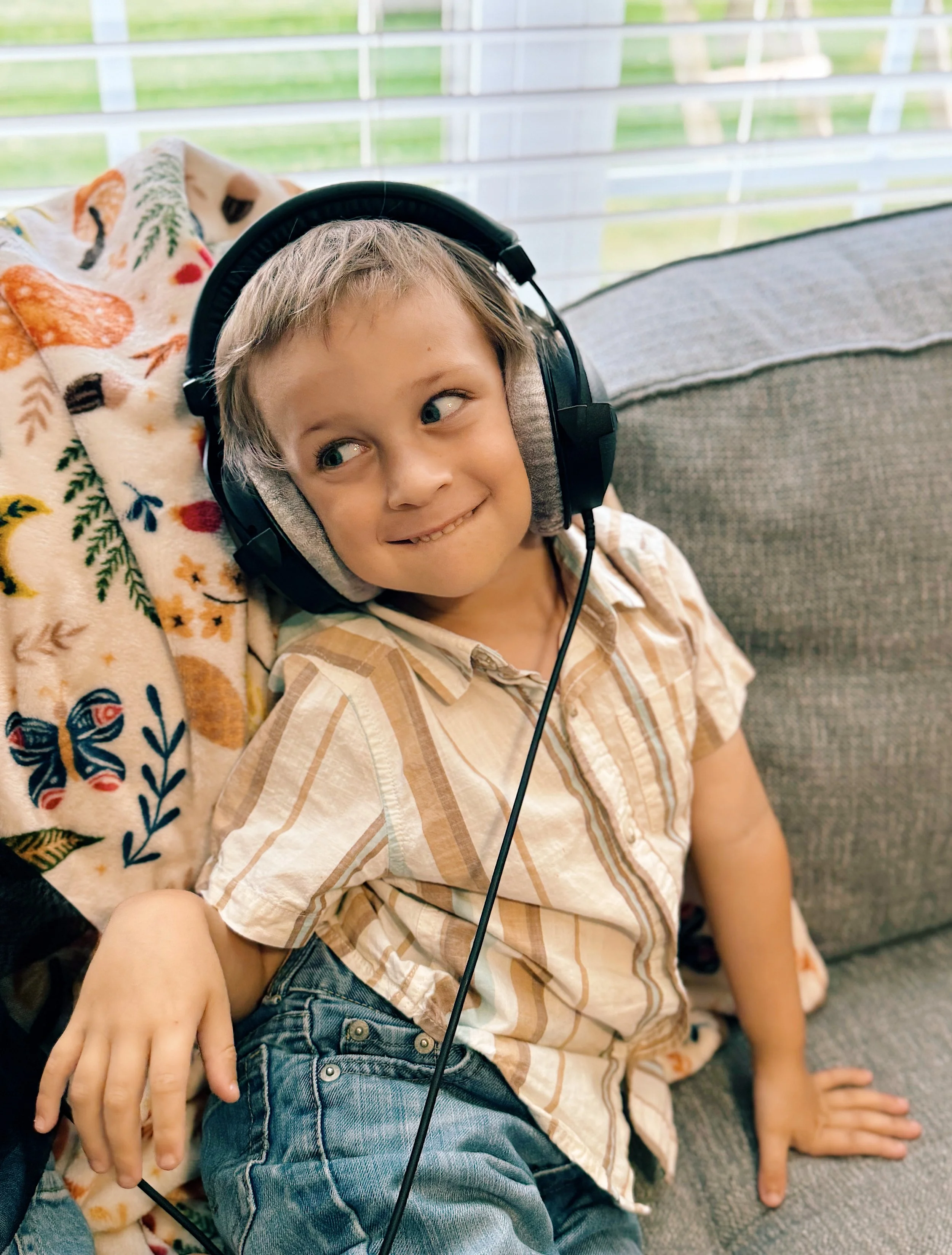 A young boy with headphones sitting on a sofa, looking to his side with a playful expression.