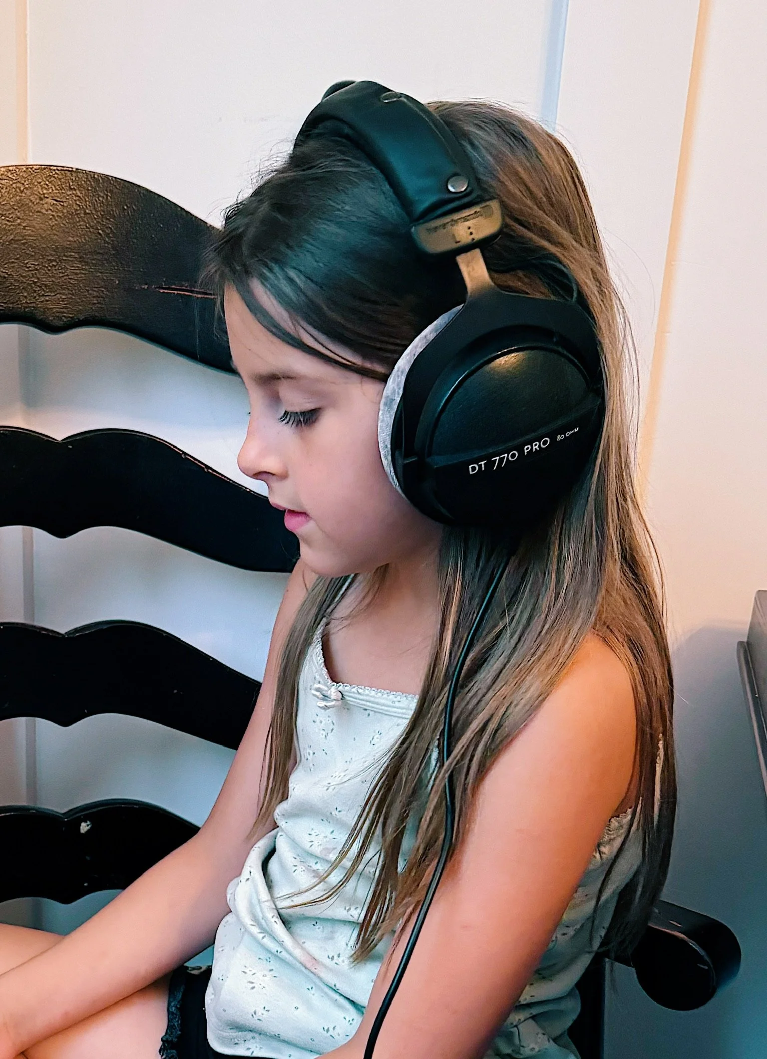 A young girl with long hair wearing large black headphones, sitting with her eyes closed.