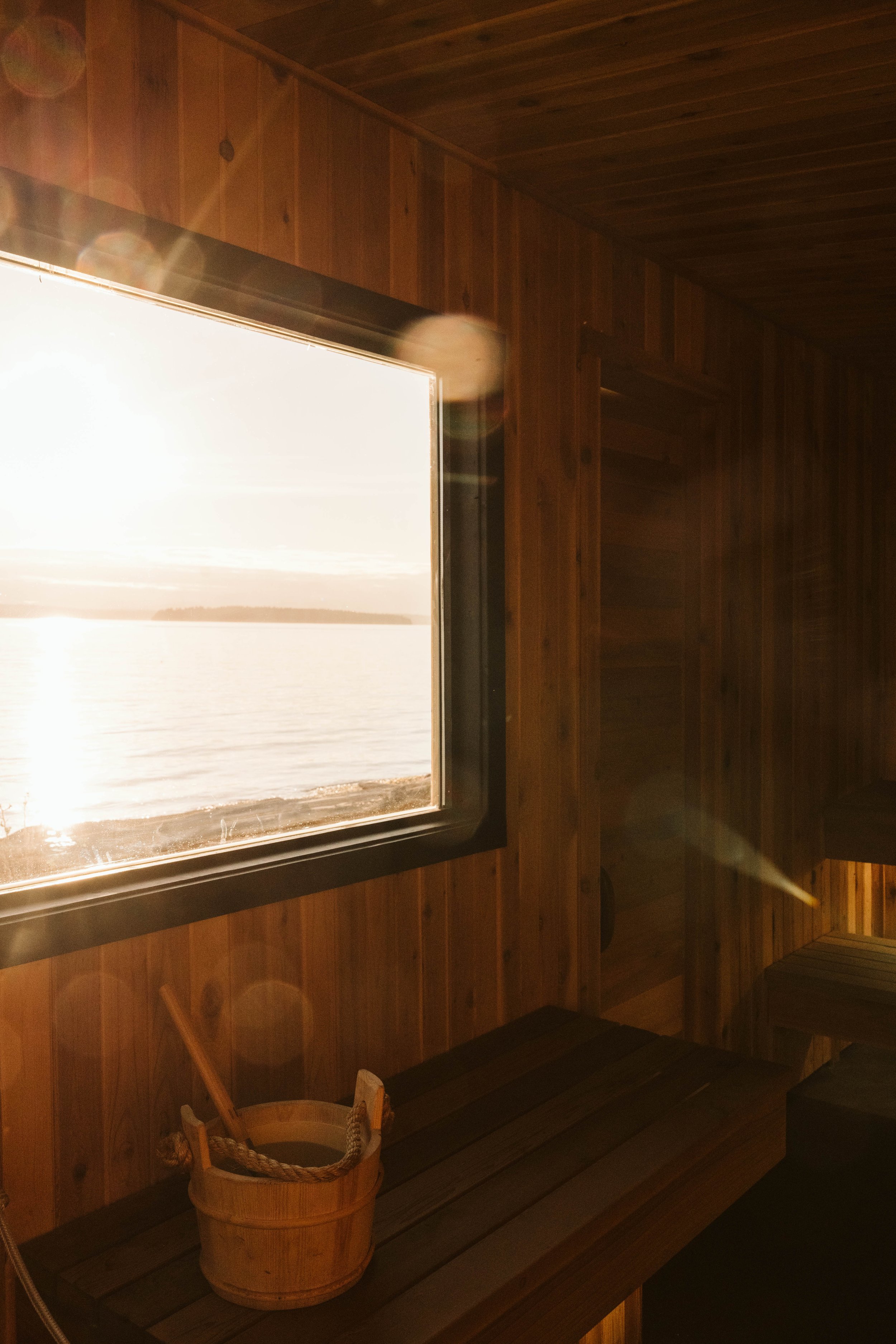 A view of a lake or ocean through an open wooden window with a wooden wall inside.