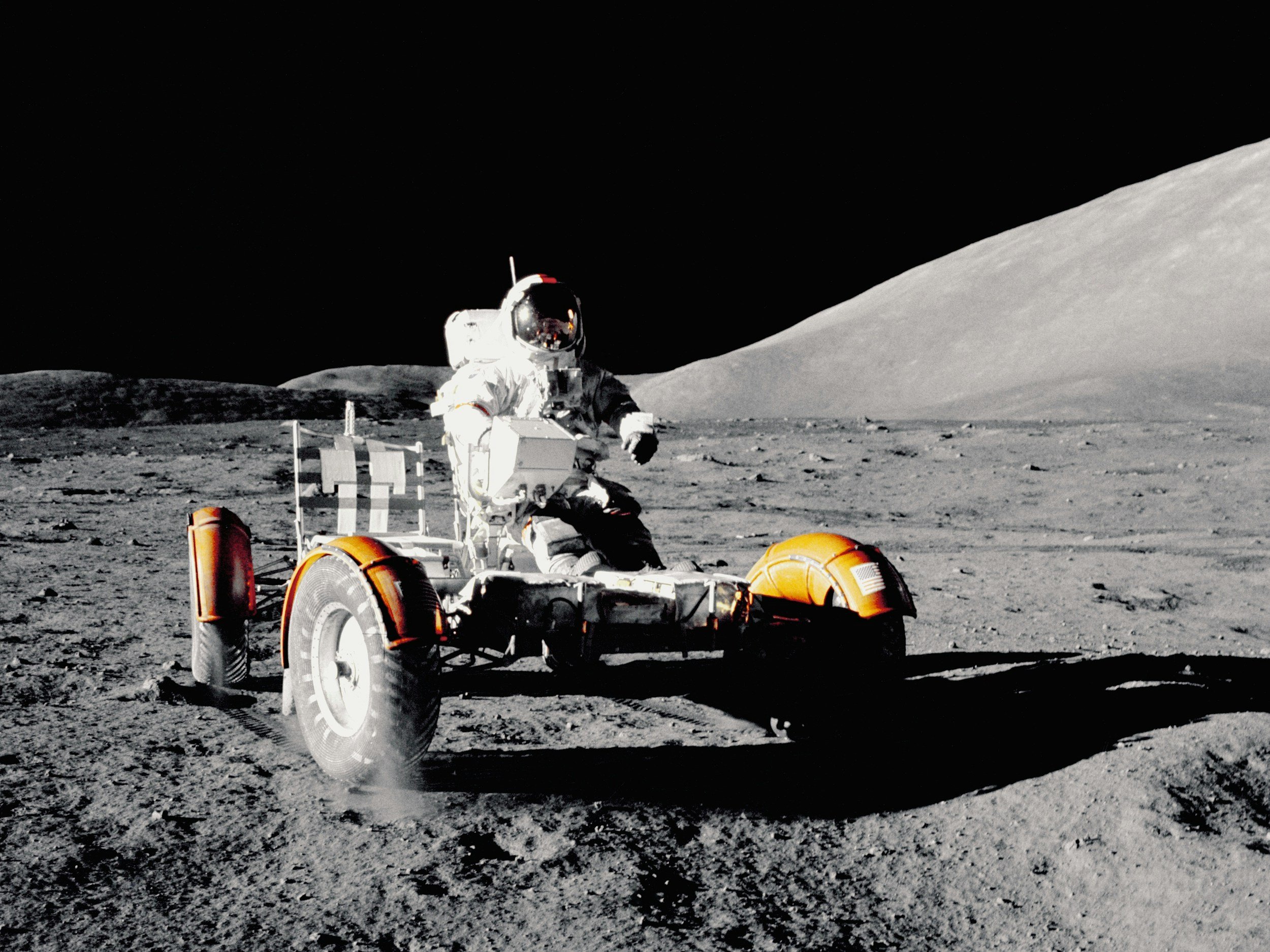 An astronaut on the moon's surface next to a lunar rover with the Earth visible in the background.