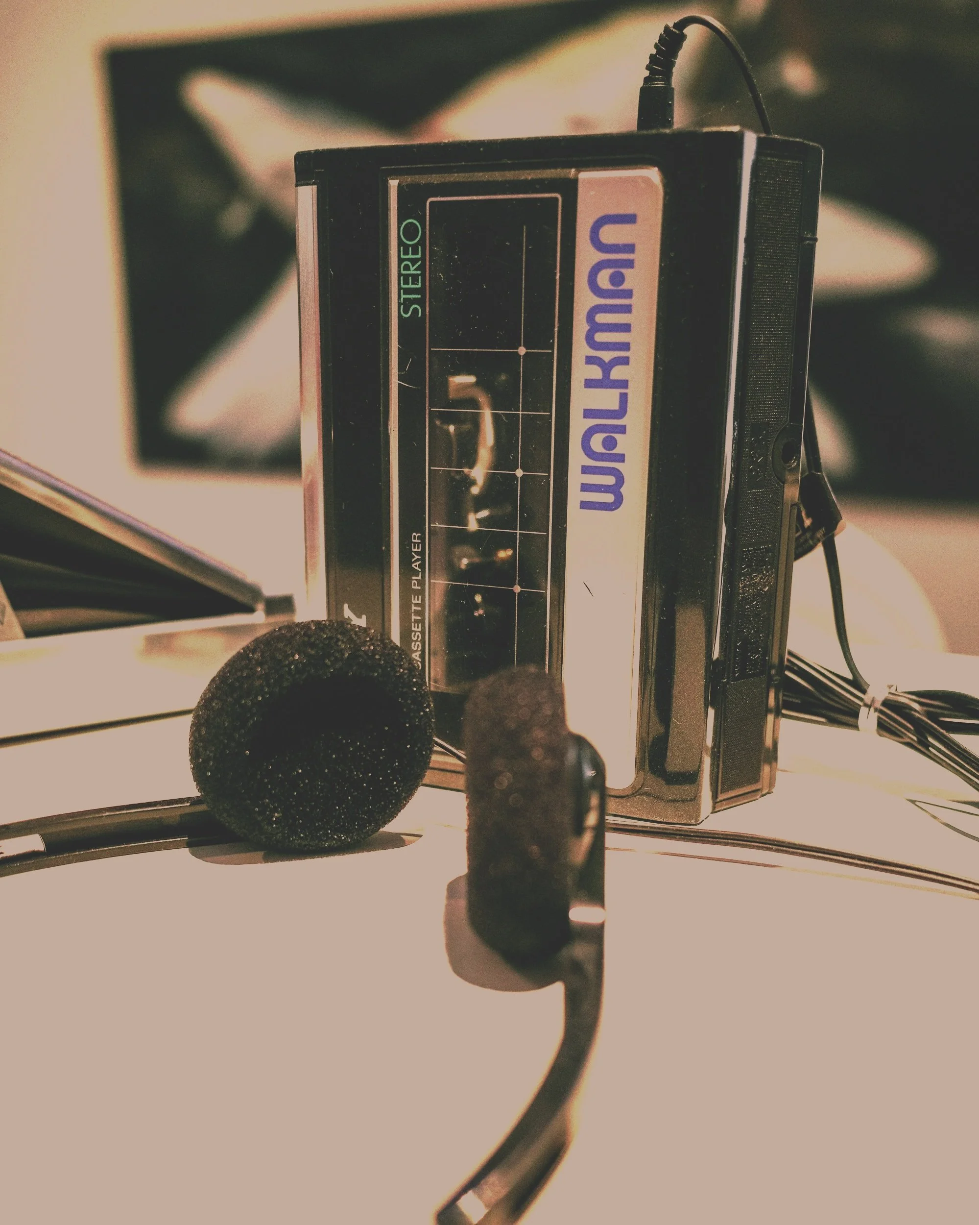 A vintage Walkman cassette player with black ear microphones on a white surface.