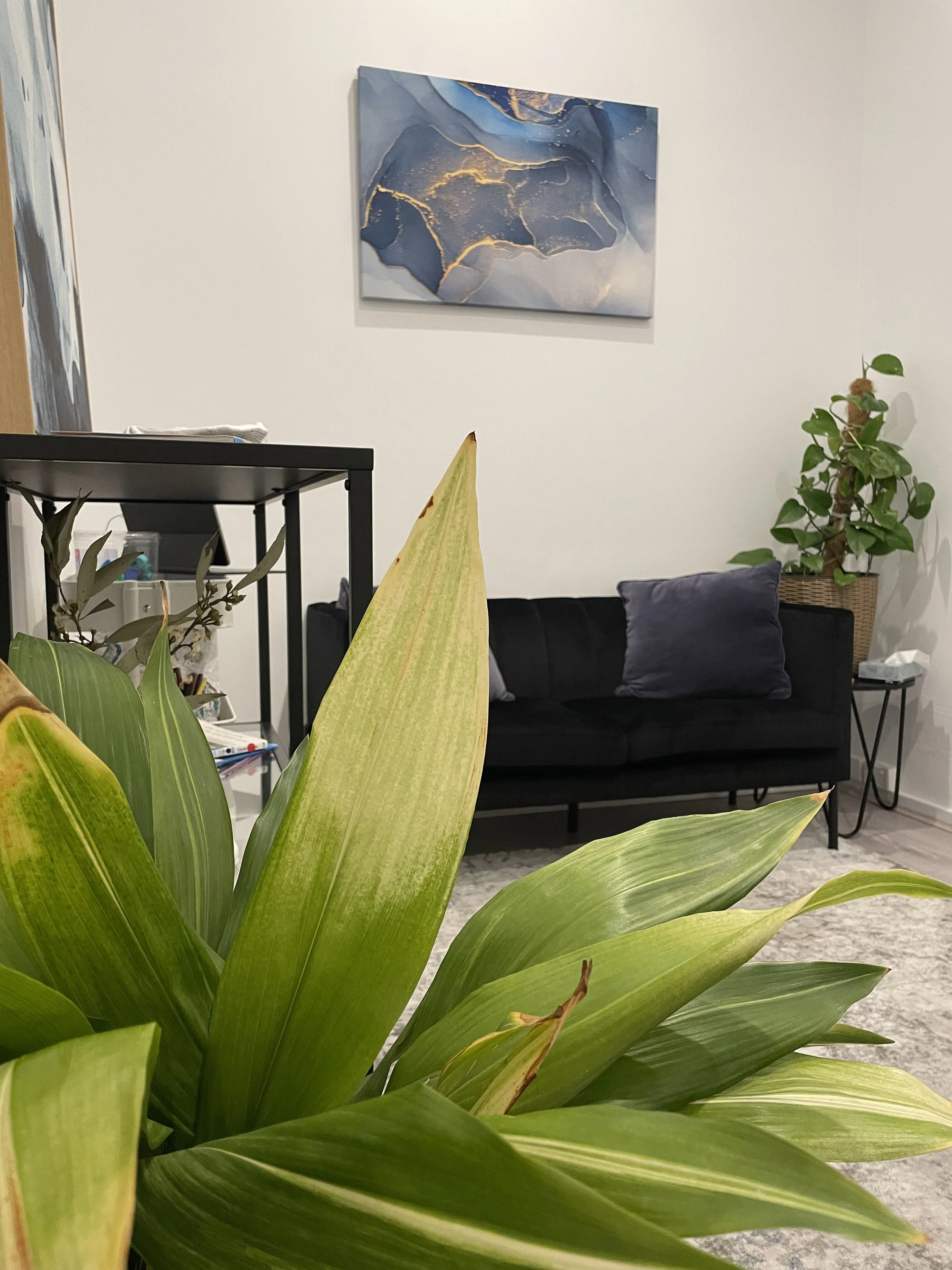 Modern living room with a teal sofa, black and gray pillows, abstract artwork, wooden accent wall, and a marble coffee table with a black bowl and white spherical decor.