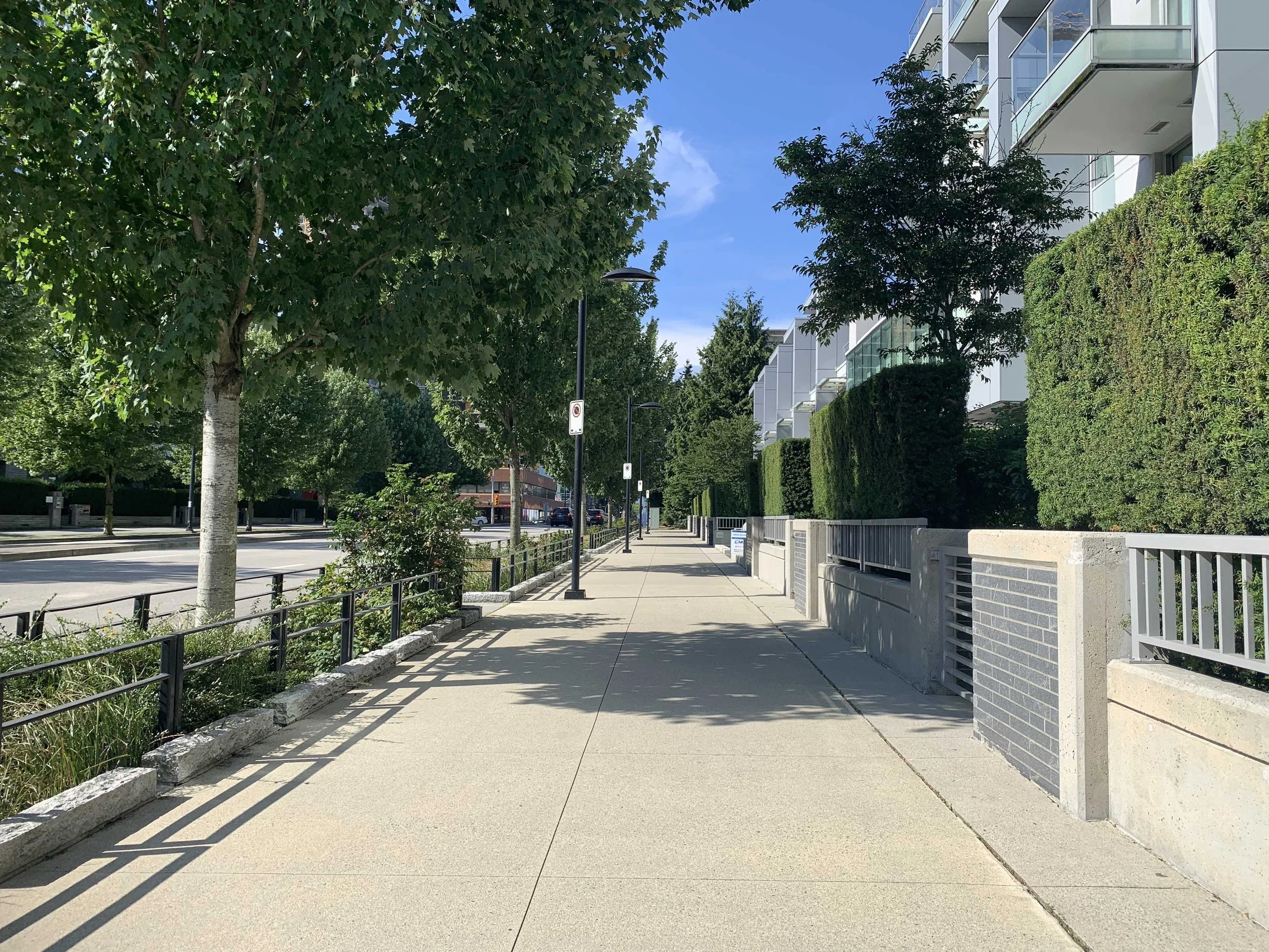 Empty sidewalk alongside modern apartment buildings and greenery on a sunny day