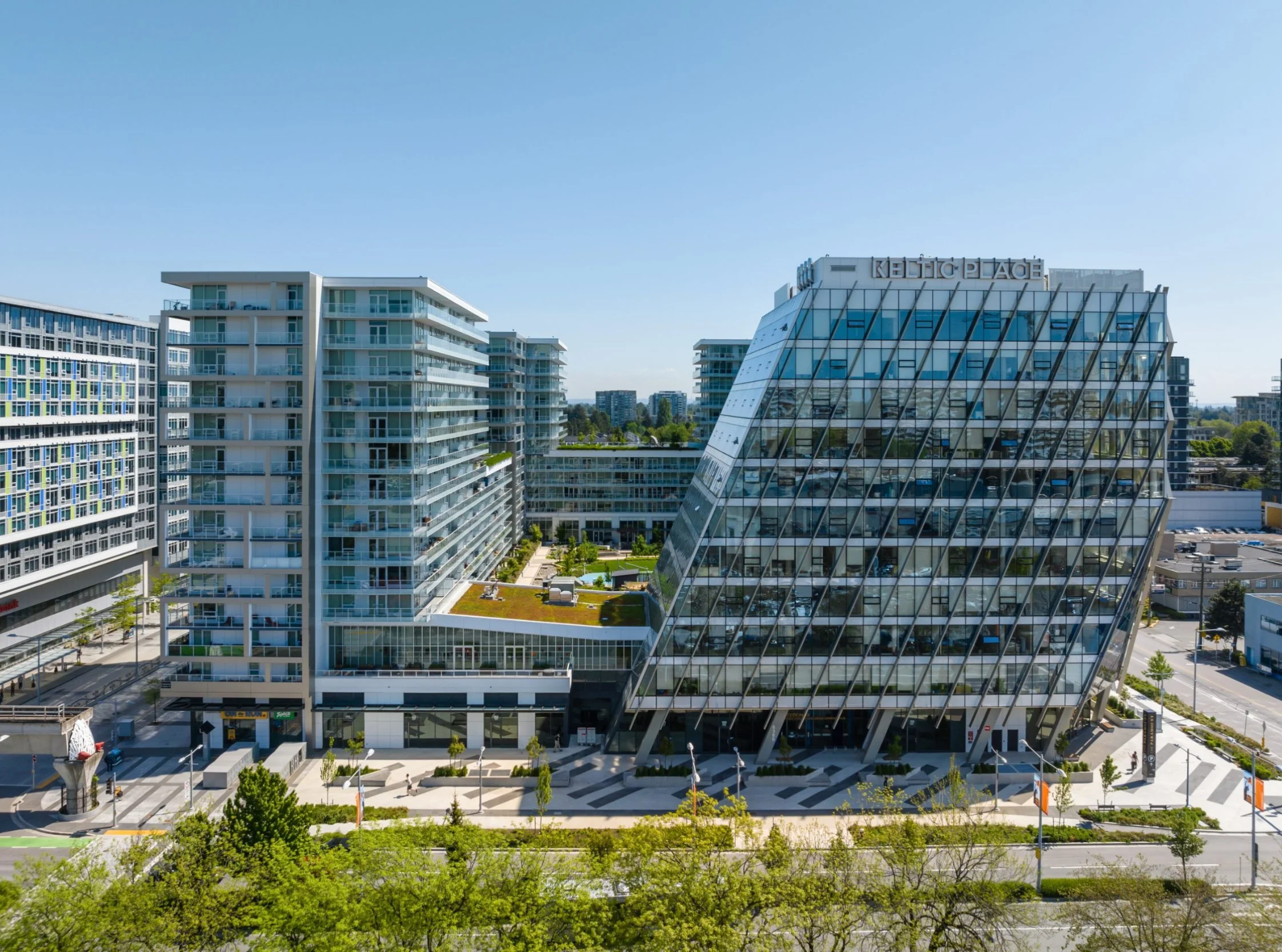 Modern glass office buildings and apartments in an urban setting with a clear blue sky.