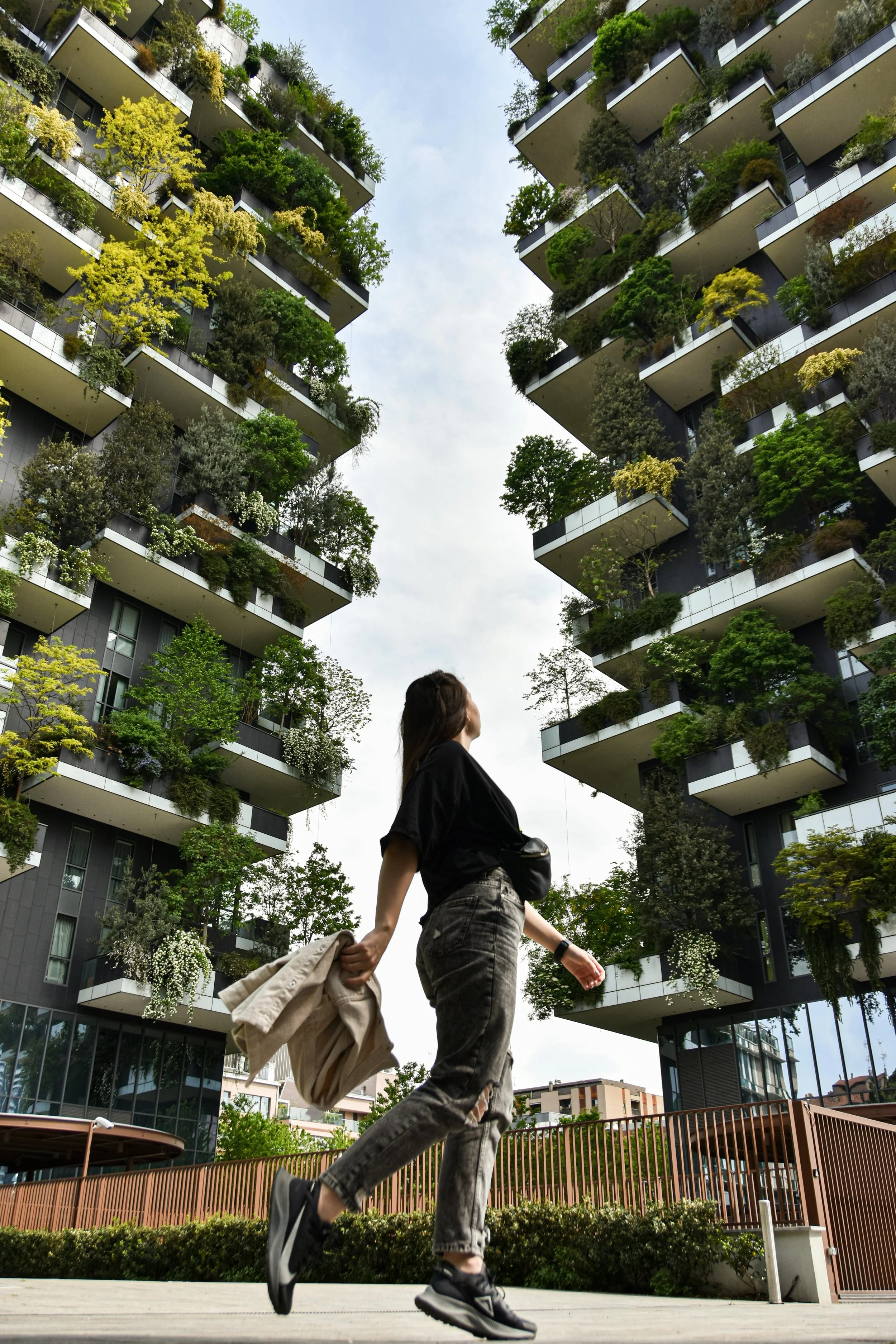 A woman walking outdoors near a modern building with lush greenery on its balconies.