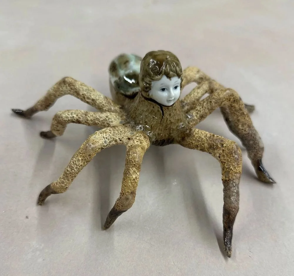 A clay spider with a face of a porcelain figurine and lava glazed legs