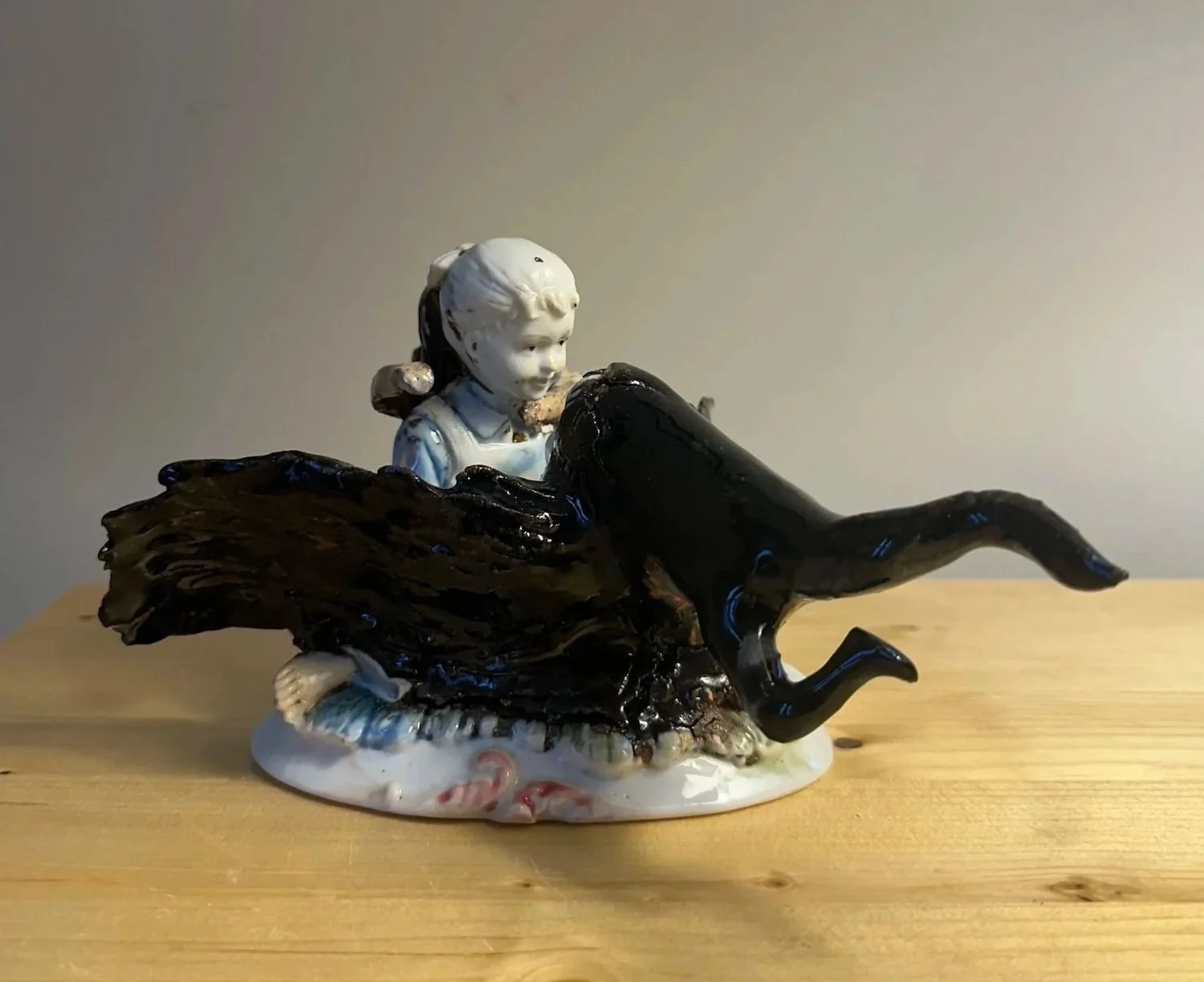 Porcelain figurine of a young girl with a black chimera on a wooden surface.