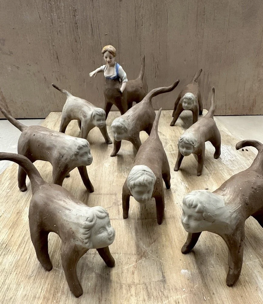 A collection of clay sculptures depicting children and animals, with one child figure standing among the animals on a wooden surface.