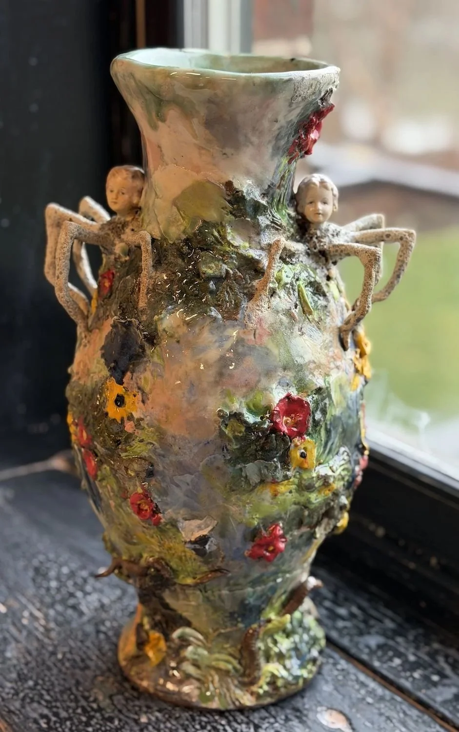 Ceramic vase decorated with small figurines of children and textured, colorful surface resembling flowers and plants.