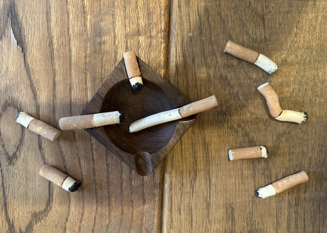 A wooden table with a small wooden bowl and several cigarette butts scattered around.