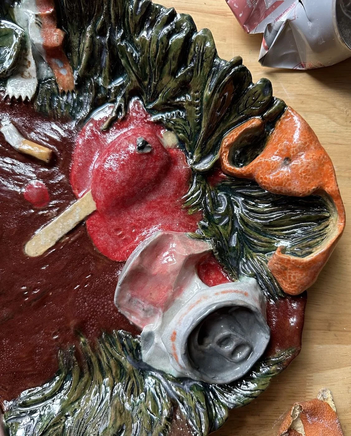 Detail of a trompe l'oeil ceramic platter with orange peel, melting Popsicle, and crushed can