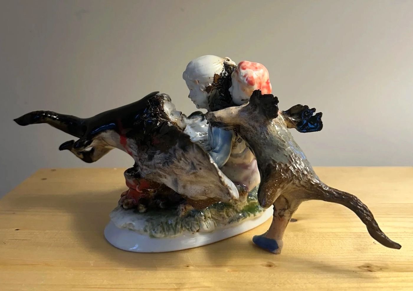 Ceramic sculpture of two fighting dogs with a person between them, on a wooden surface.