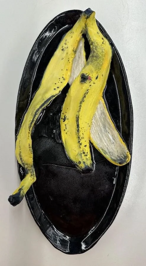 A black oval serving tray with a ceramic trompe l'oeil banana peel