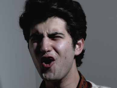Close-up of a young man making a funny face with puckered lips and furrowed brows.