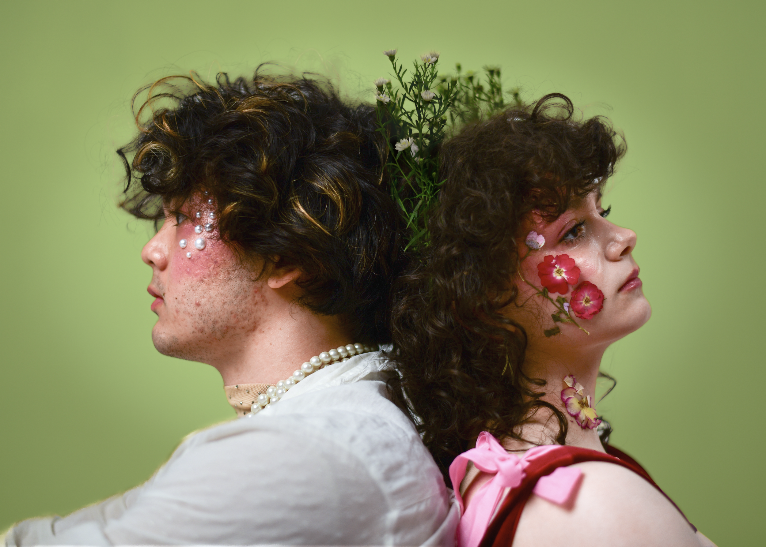 Side profile of two people standing back to back with flowers and greenery on their faces and head against a light green background.