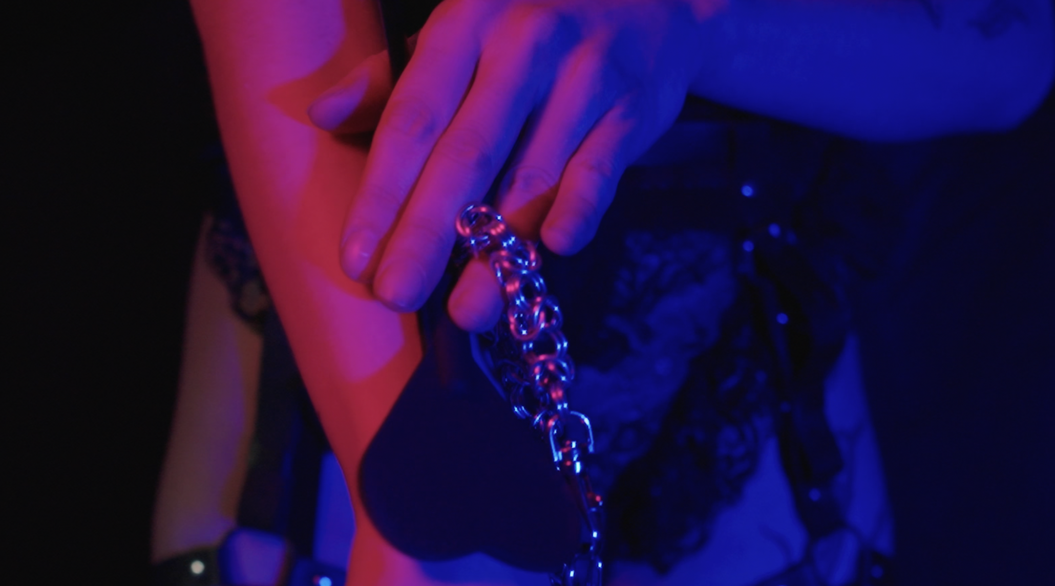 A person's hand holding a chain with large links, illuminated by purple and blue lighting.