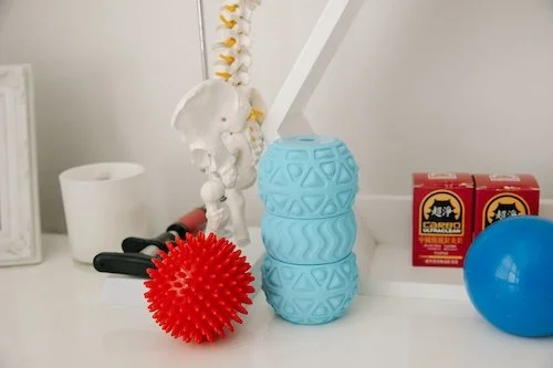 Medical or therapy workspace with a red spiky massage ball, a blue textured massage ball, a model of the human spine, and boxes of Bear brand herbal products.