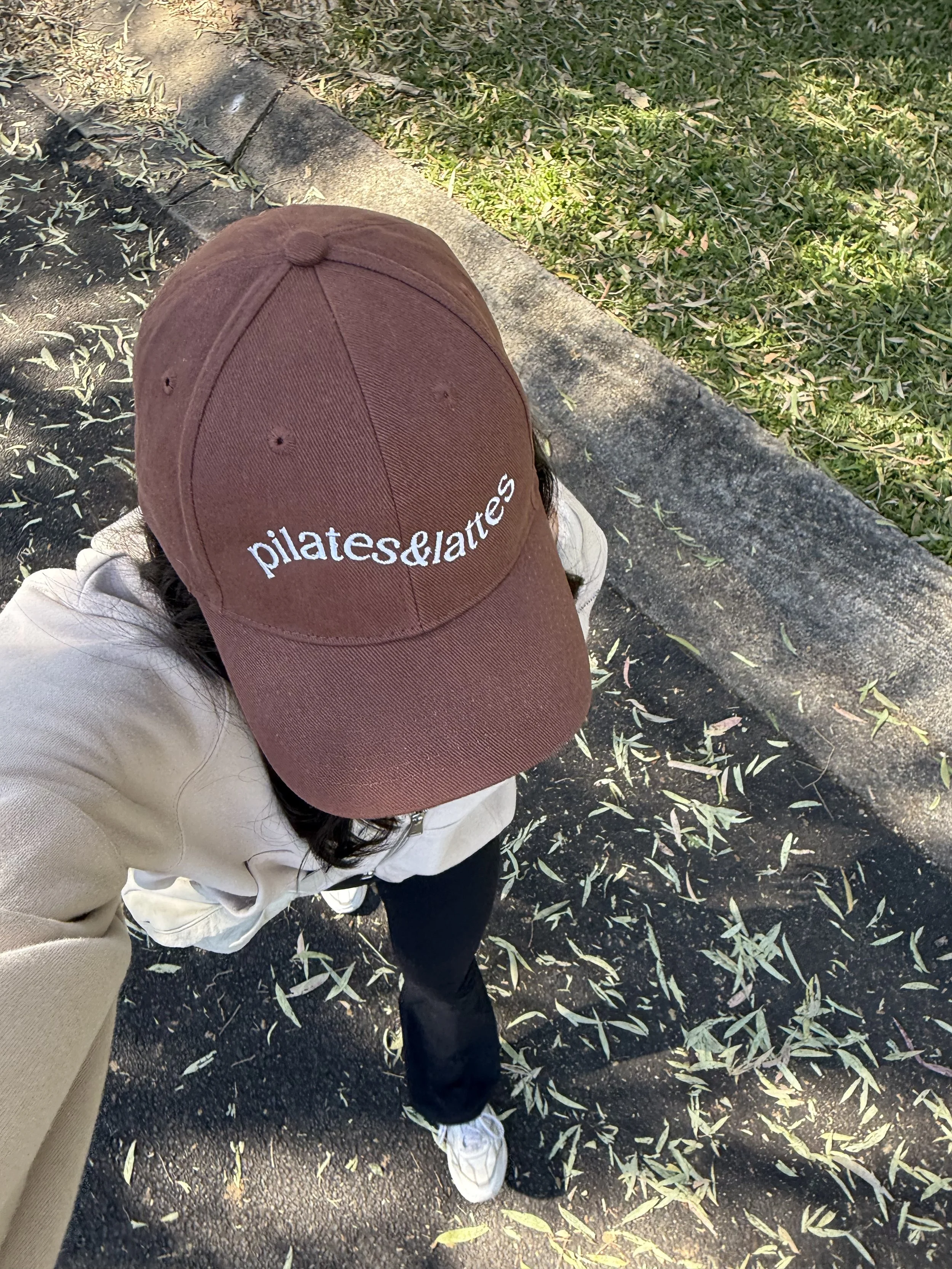 Girl out walking wearing pilates and lattes hat, which is brown with embroidered text