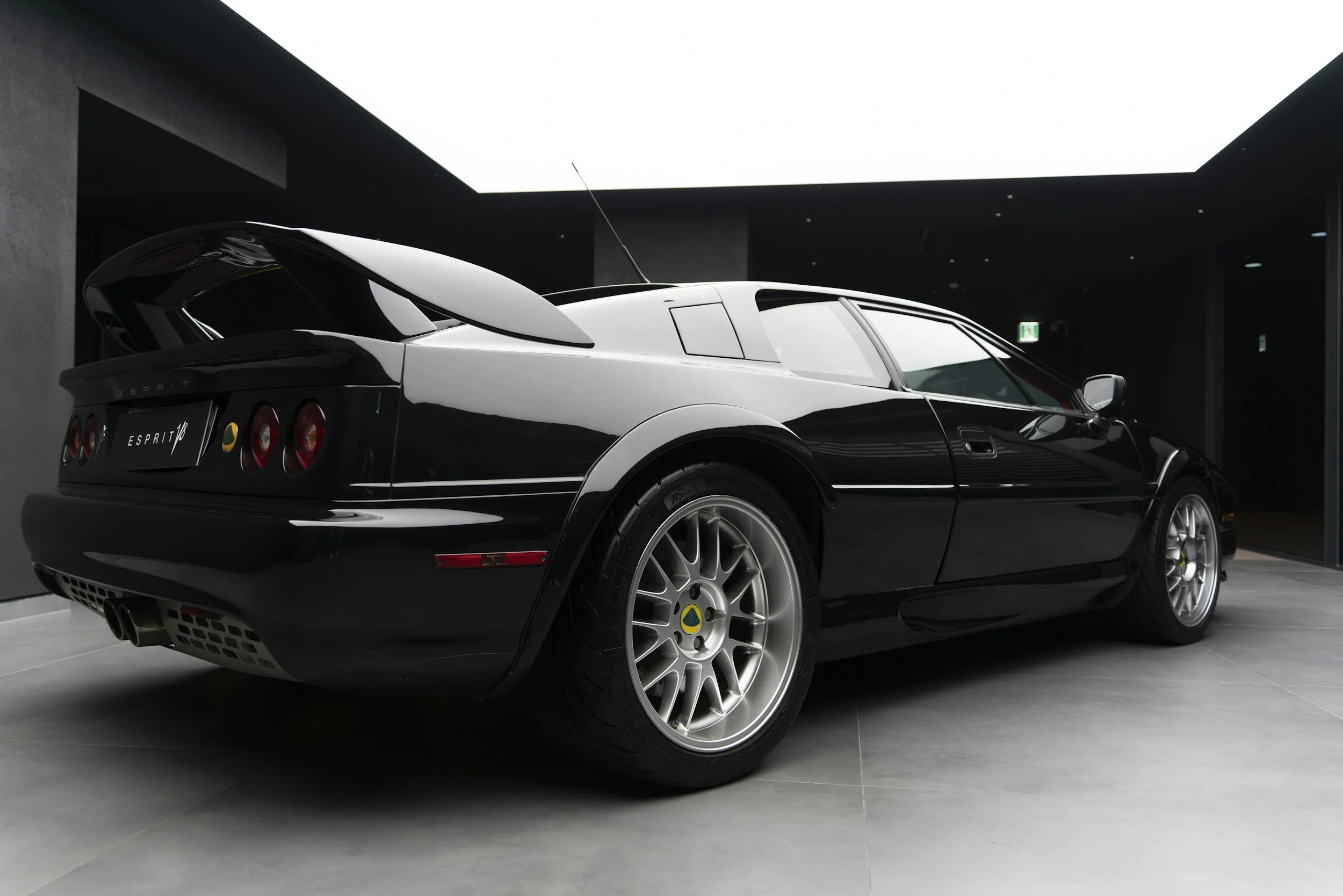 A black and white Lotus Esprit sports car inside a modern showroom with dark walls and gray tiled flooring.