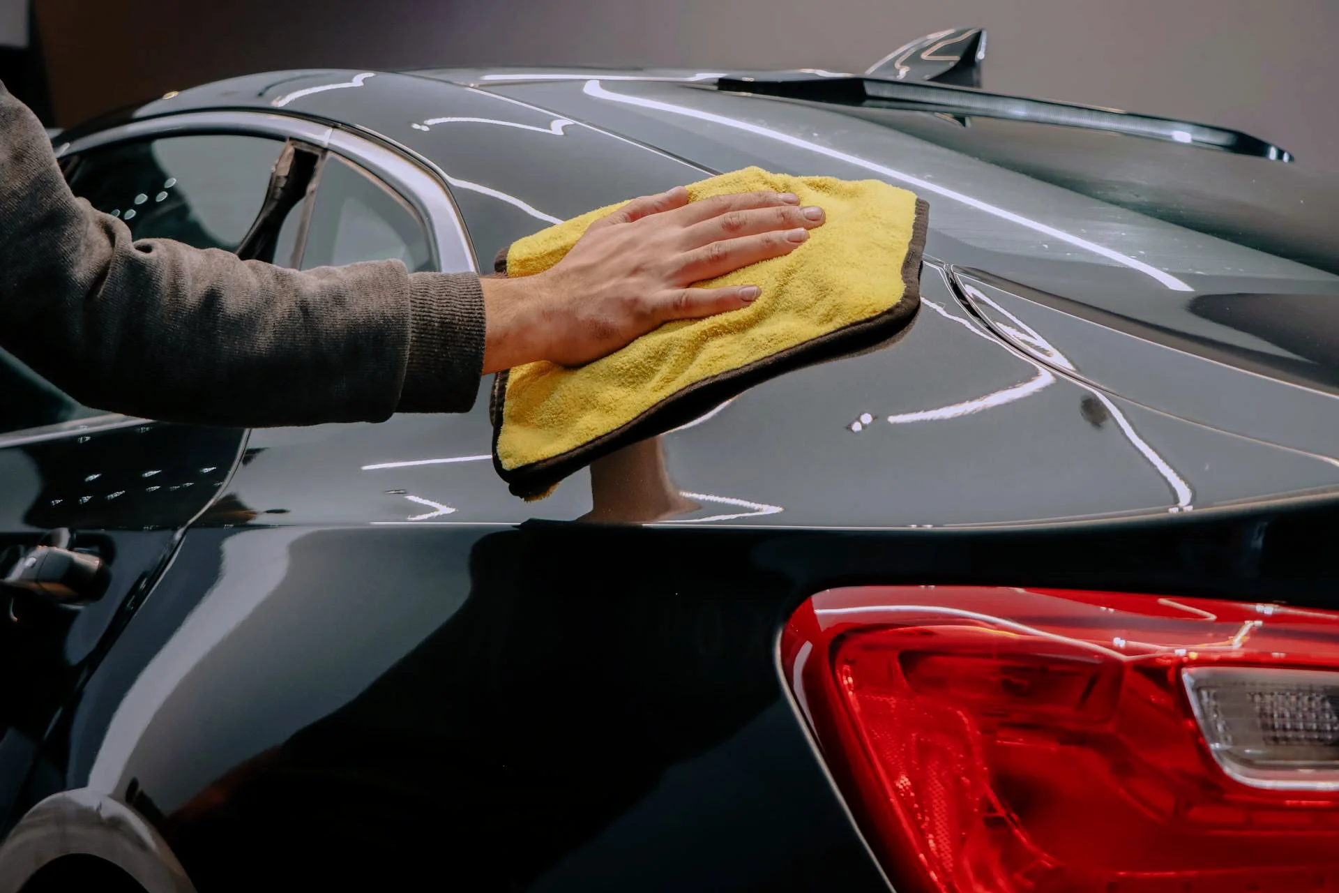 Person cleaning the trunk of a black car with a yellow cloth.
