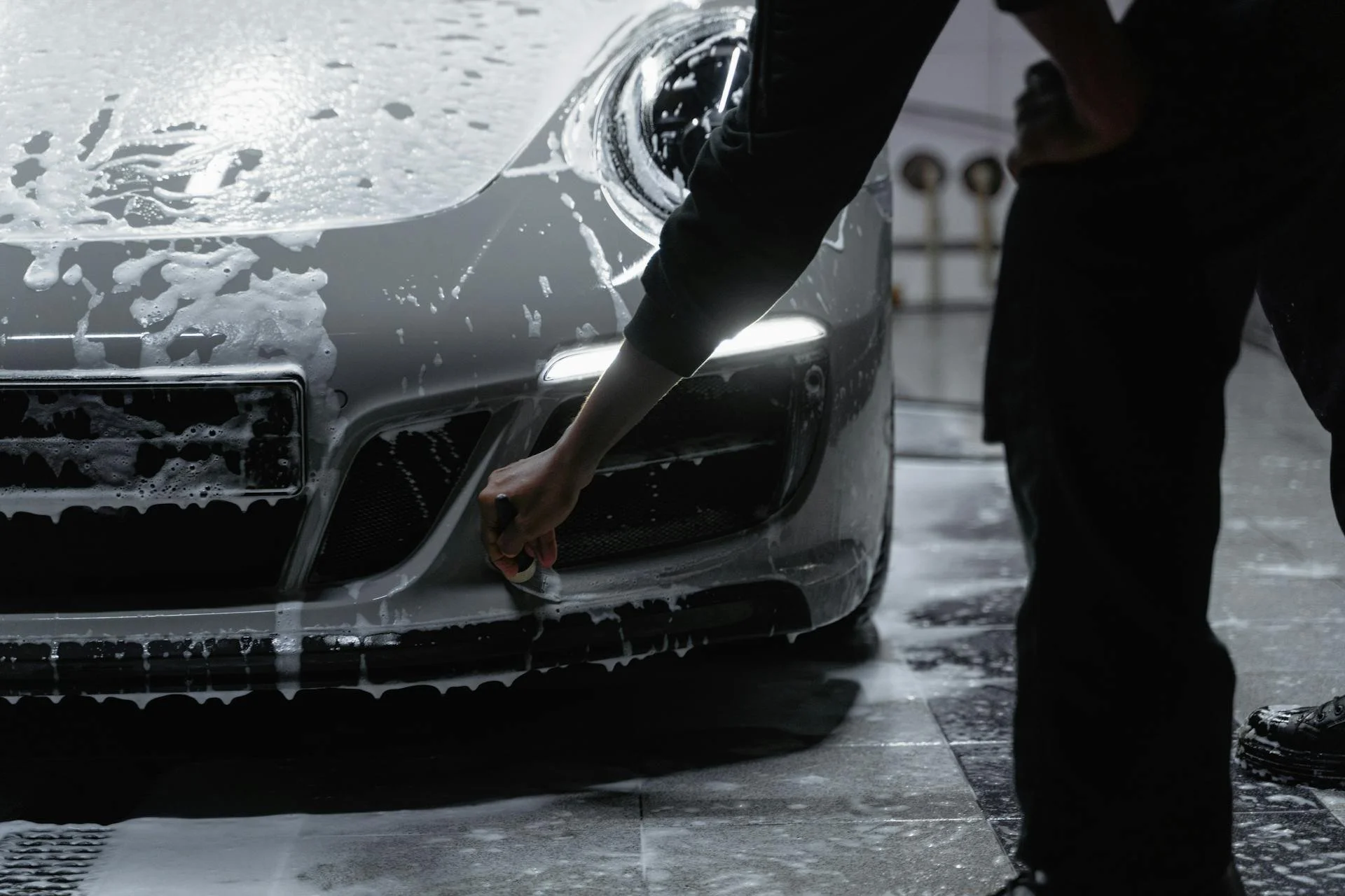Person cleaning soap off a silver car in a car wash.