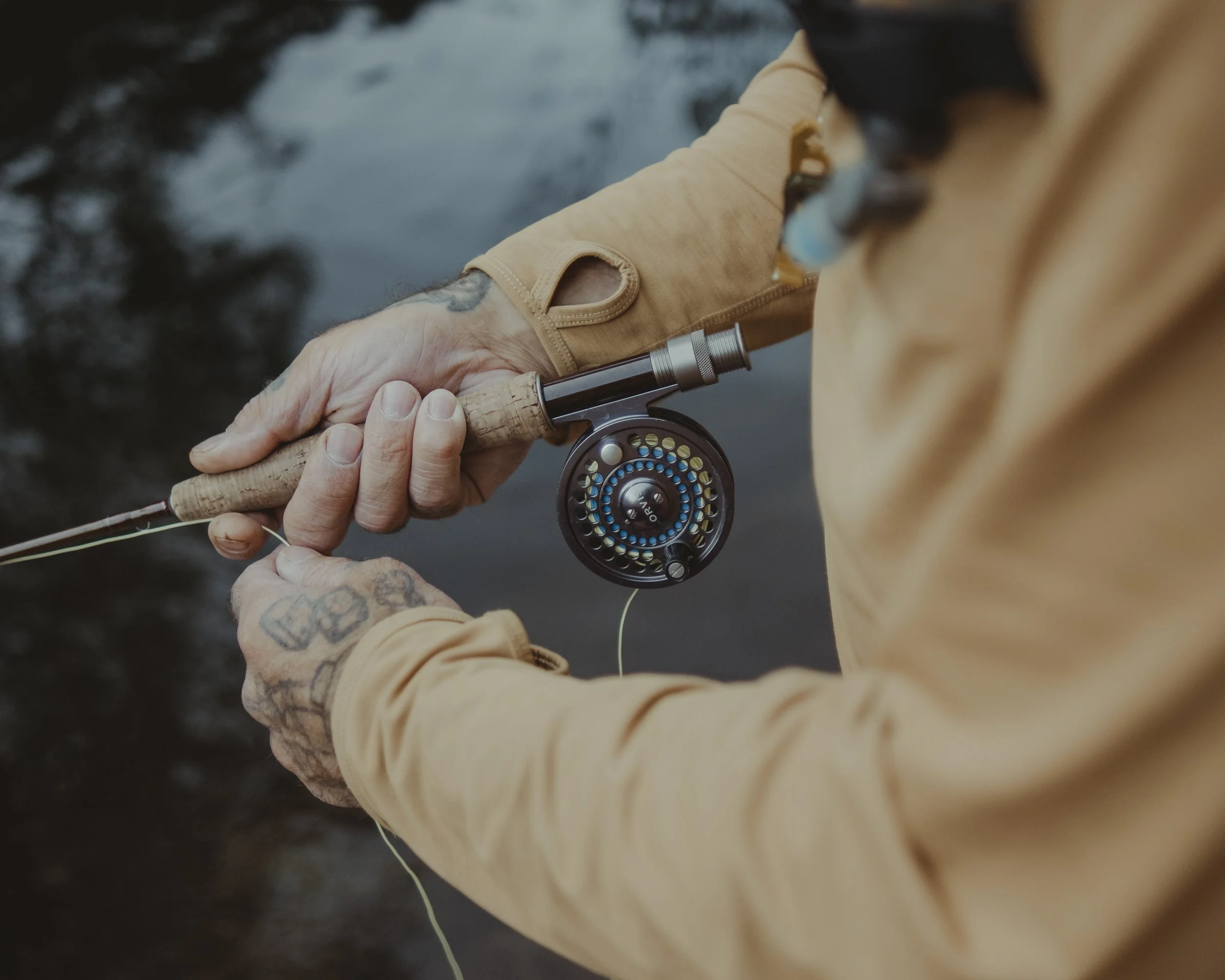 Person holding a fishing rod with a reel, casting line in a river or creek.