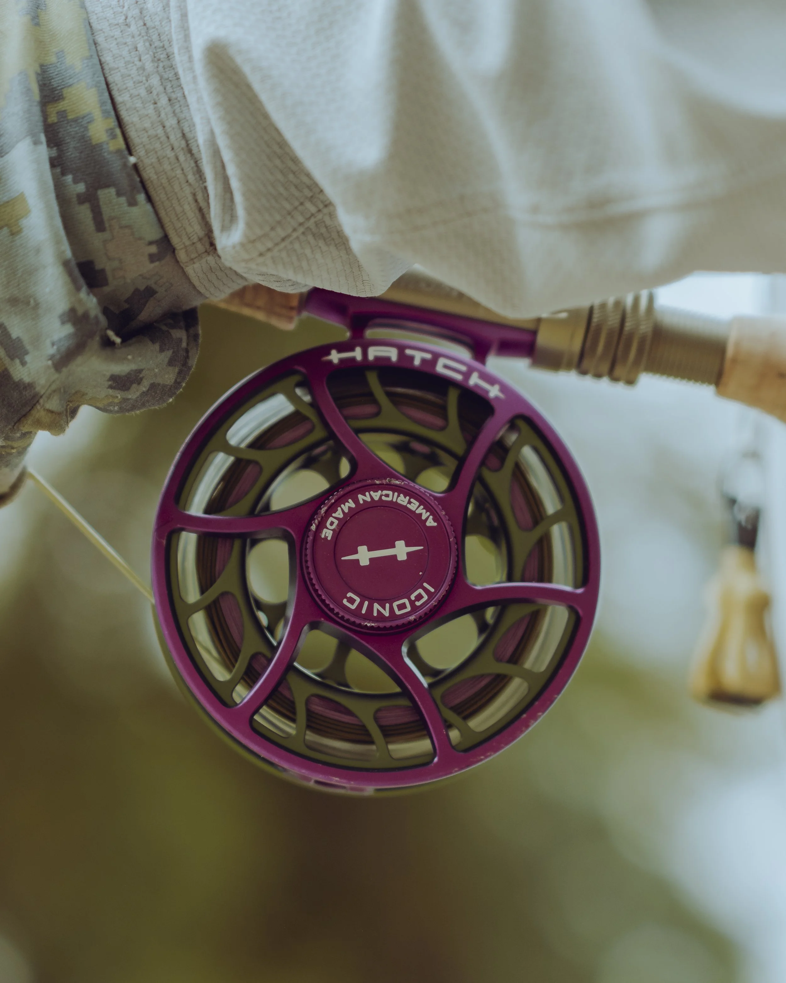 Close-up of a purple and green fly fishing reel with the brand name 'TATCH' and the words 'Liquid' and 'Made in Taiwan' visible, attached to a fishing rod.