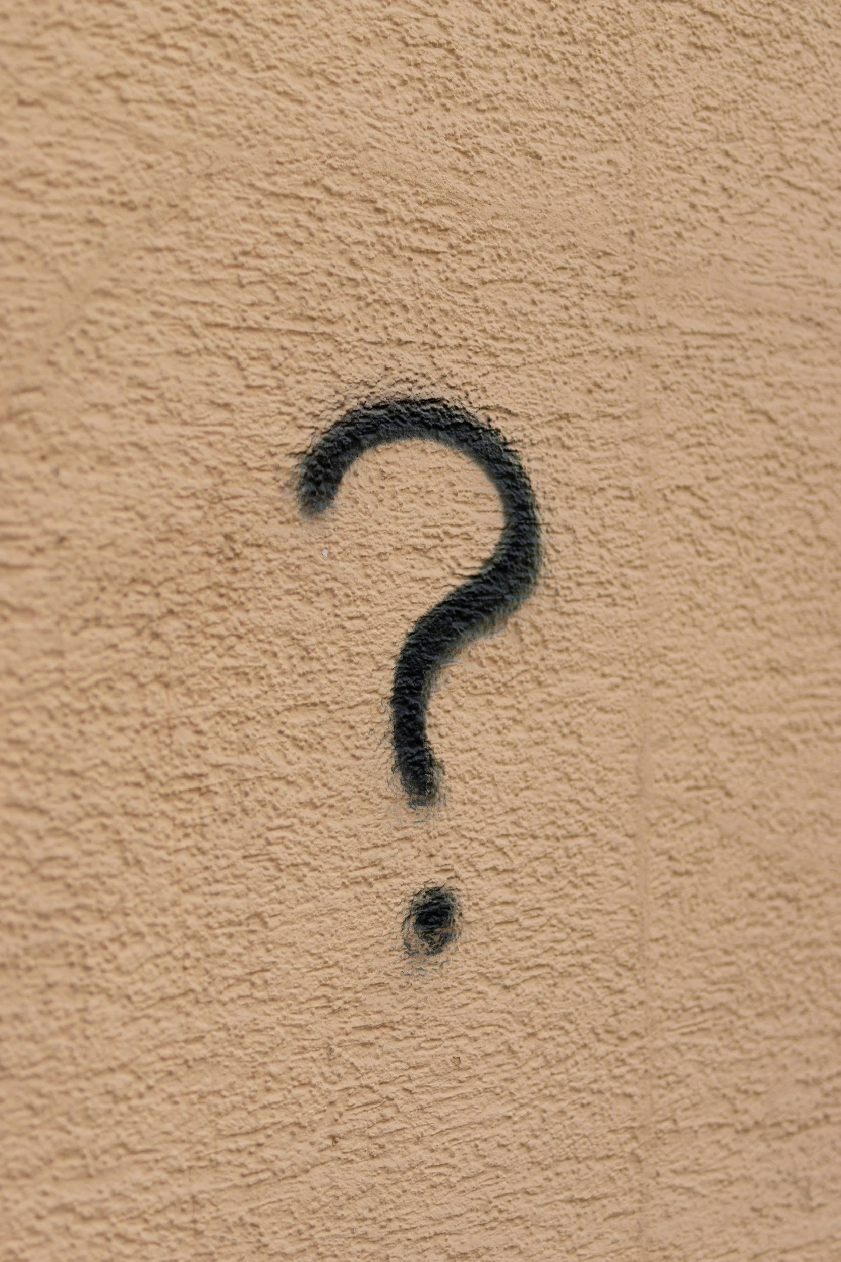 Black question mark spray-painted on a beige textured wall.
