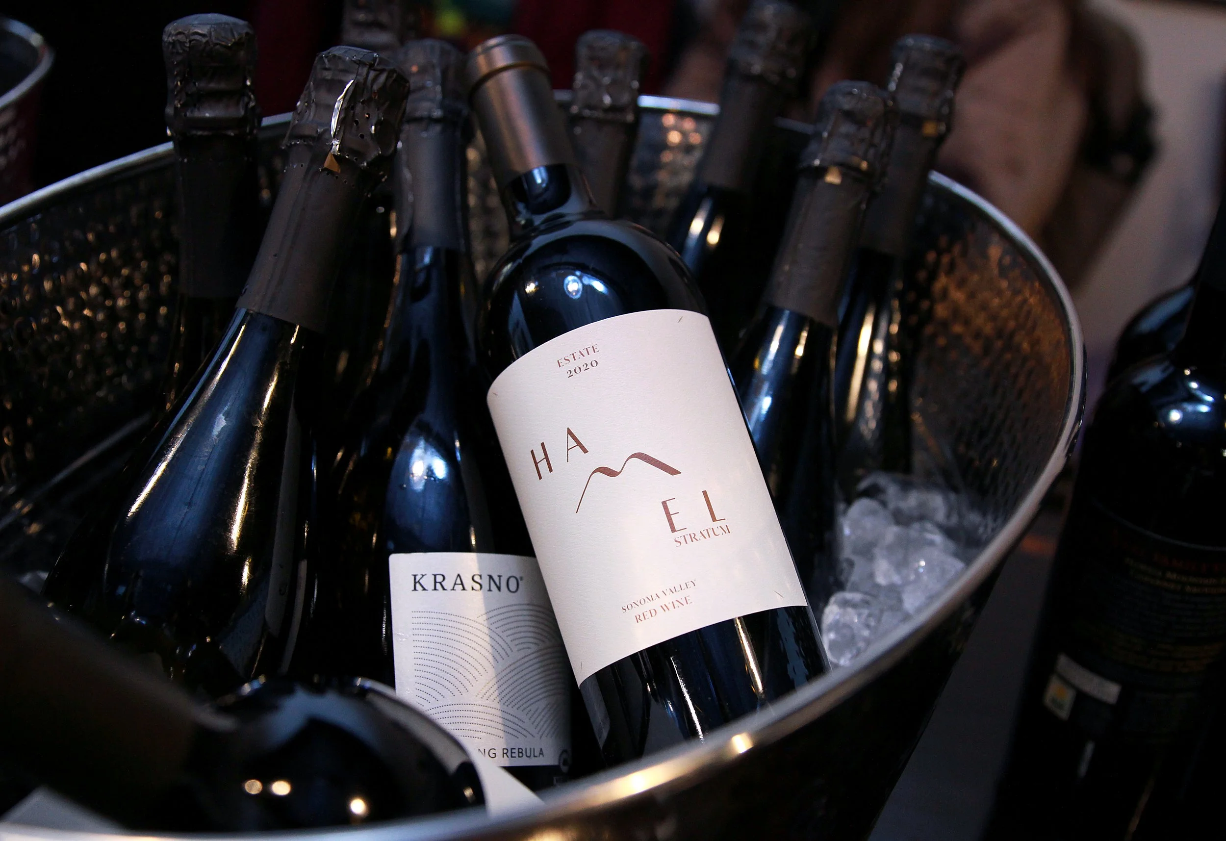 Bottles of red wine in an ice bucket, including a 2020 estate wine named 'Hale' from Sonoma Valley, surrounded by ice.