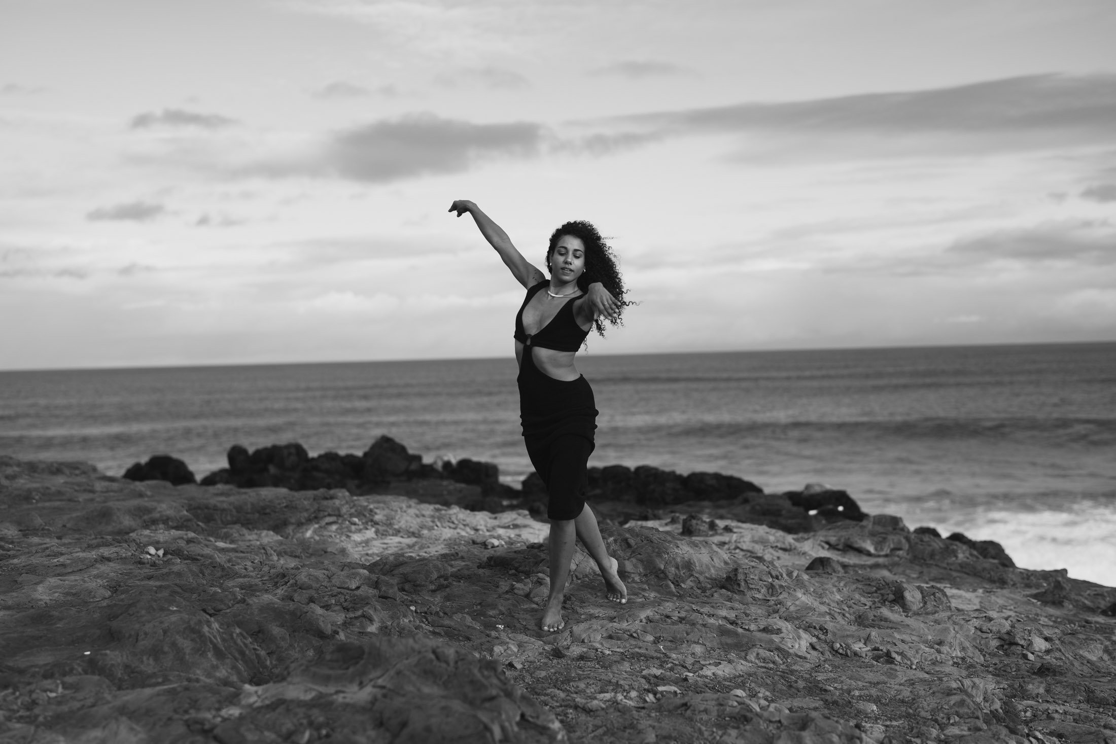 Woman dancing on rocky beach with ocean in background, black and white photo during her artistic photoshoot maui.