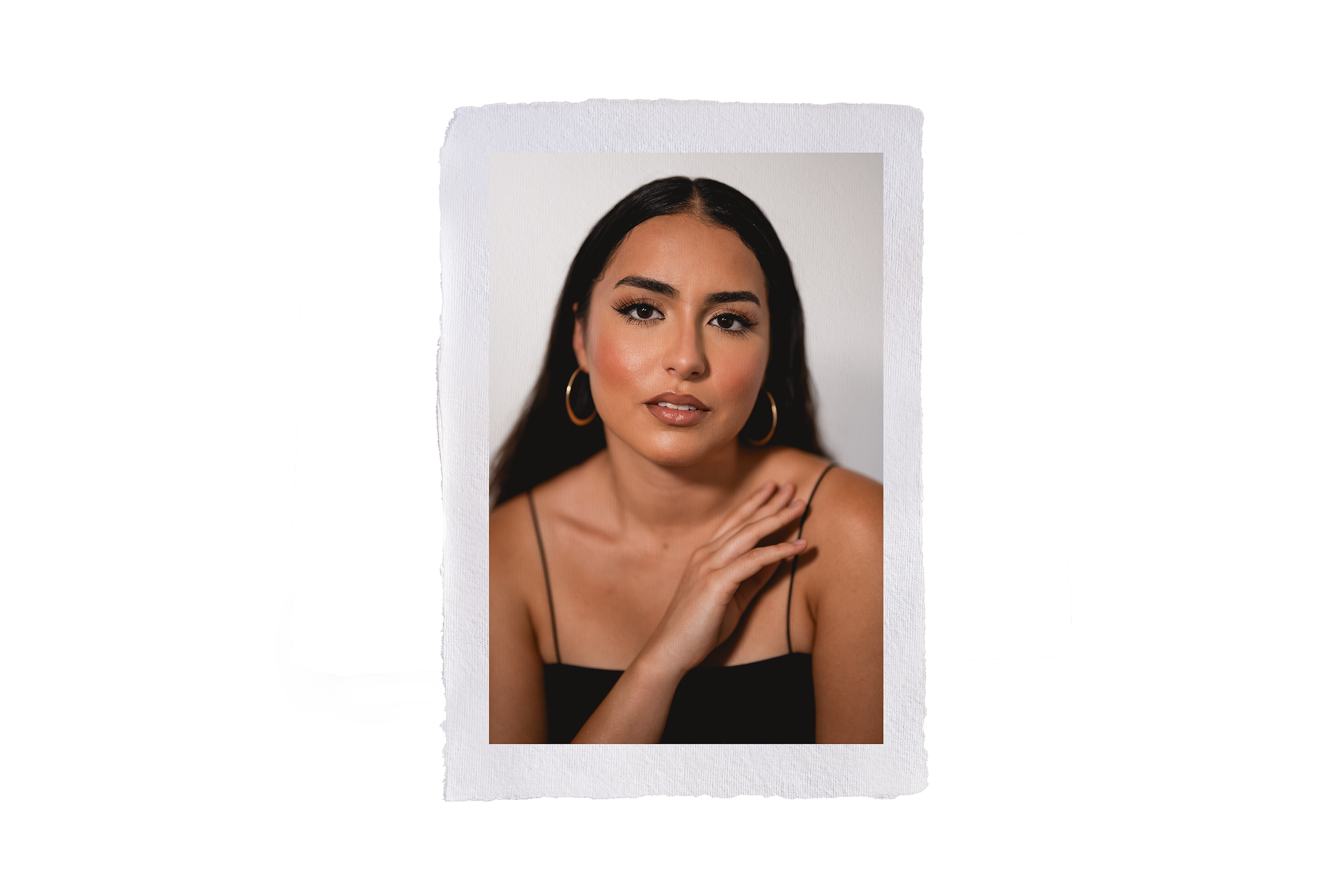 Close-up portrait of a young woman with long dark hair, hoop earrings, and a black spaghetti strap top, looking at the camera with a neutral expression, against a plain light background during a branding photoshoot maui.