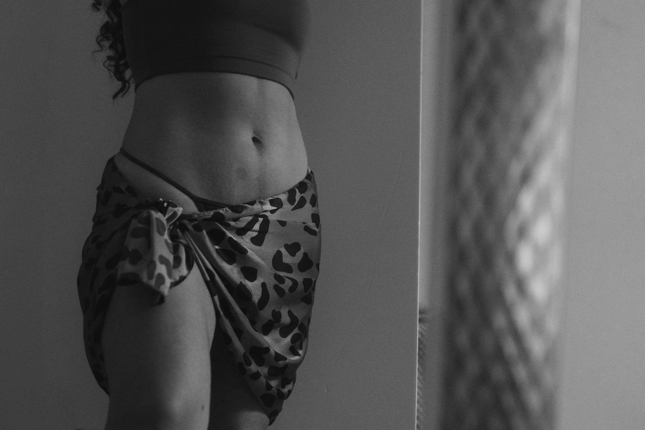 Black and white photo of a woman's midsection, showing her stomach and part of her leopard print scarf tied at the side, with her face not visible during her empowerment boudoir session.
