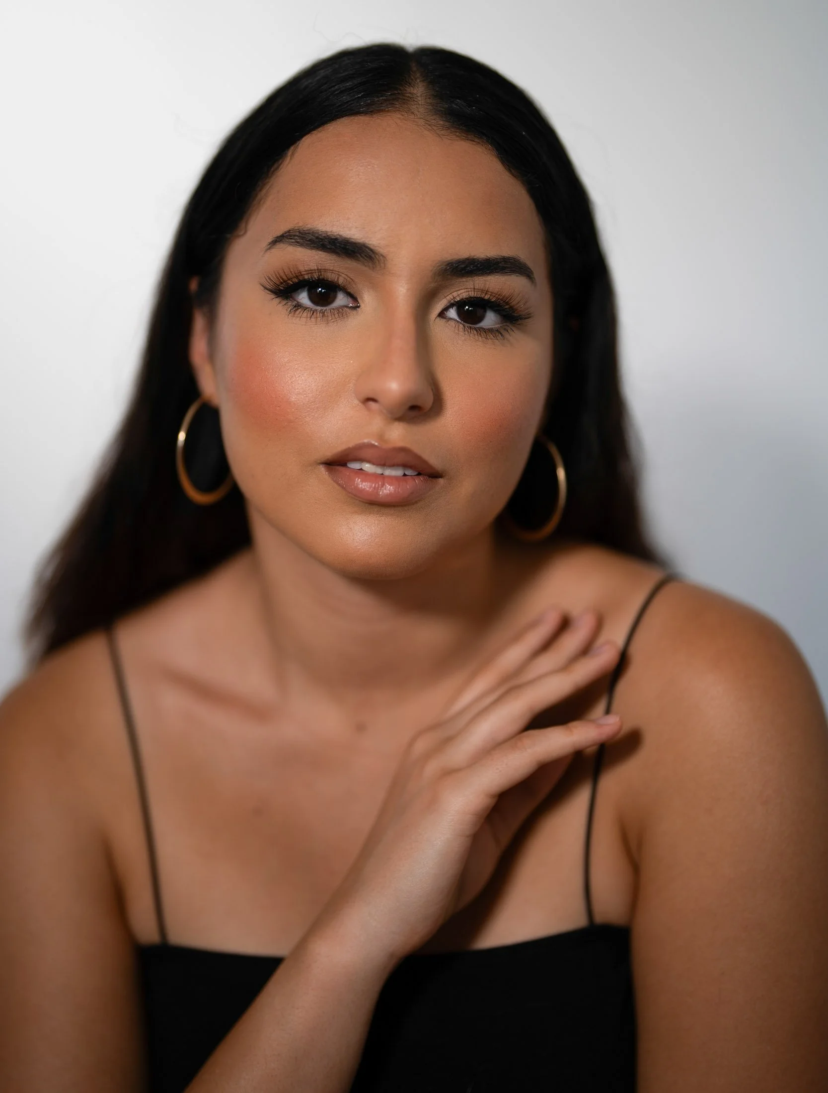 A woman with dark hair, wearing gold hoop earrings and a black spaghetti strap top, looking at the camera with her hand resting on her shoulder for her branding photoshoot maui.