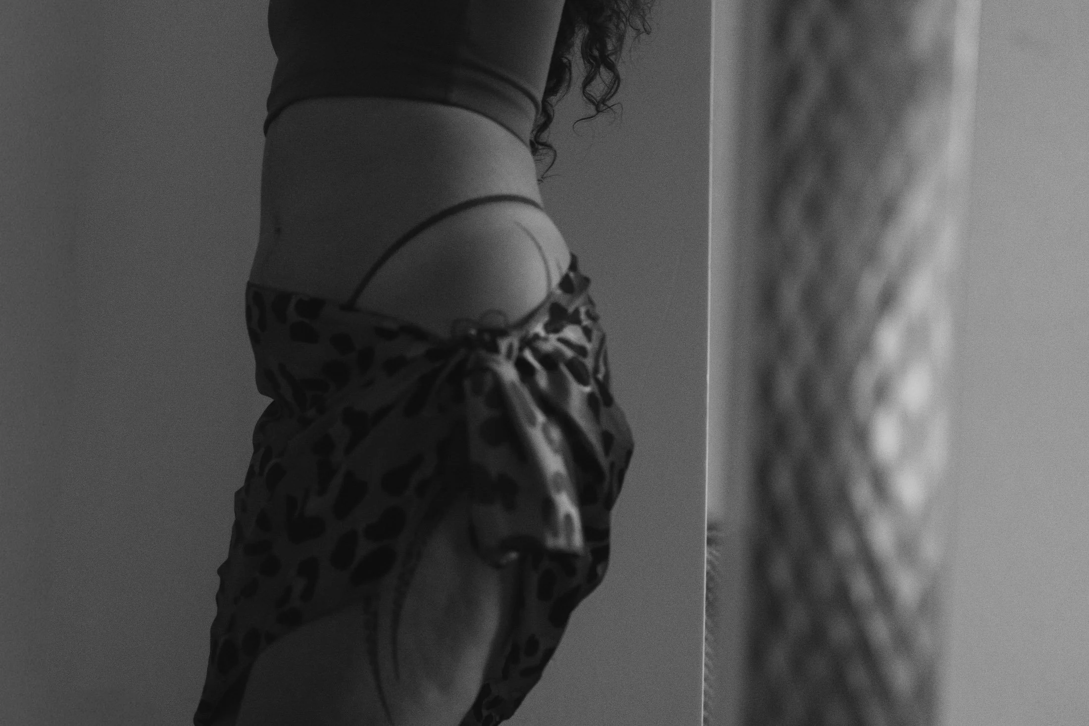 A person standing in front of a mirror, wearing a sports bra and leopard scarf, with their reflection partially visible for their intimate portrait photography.