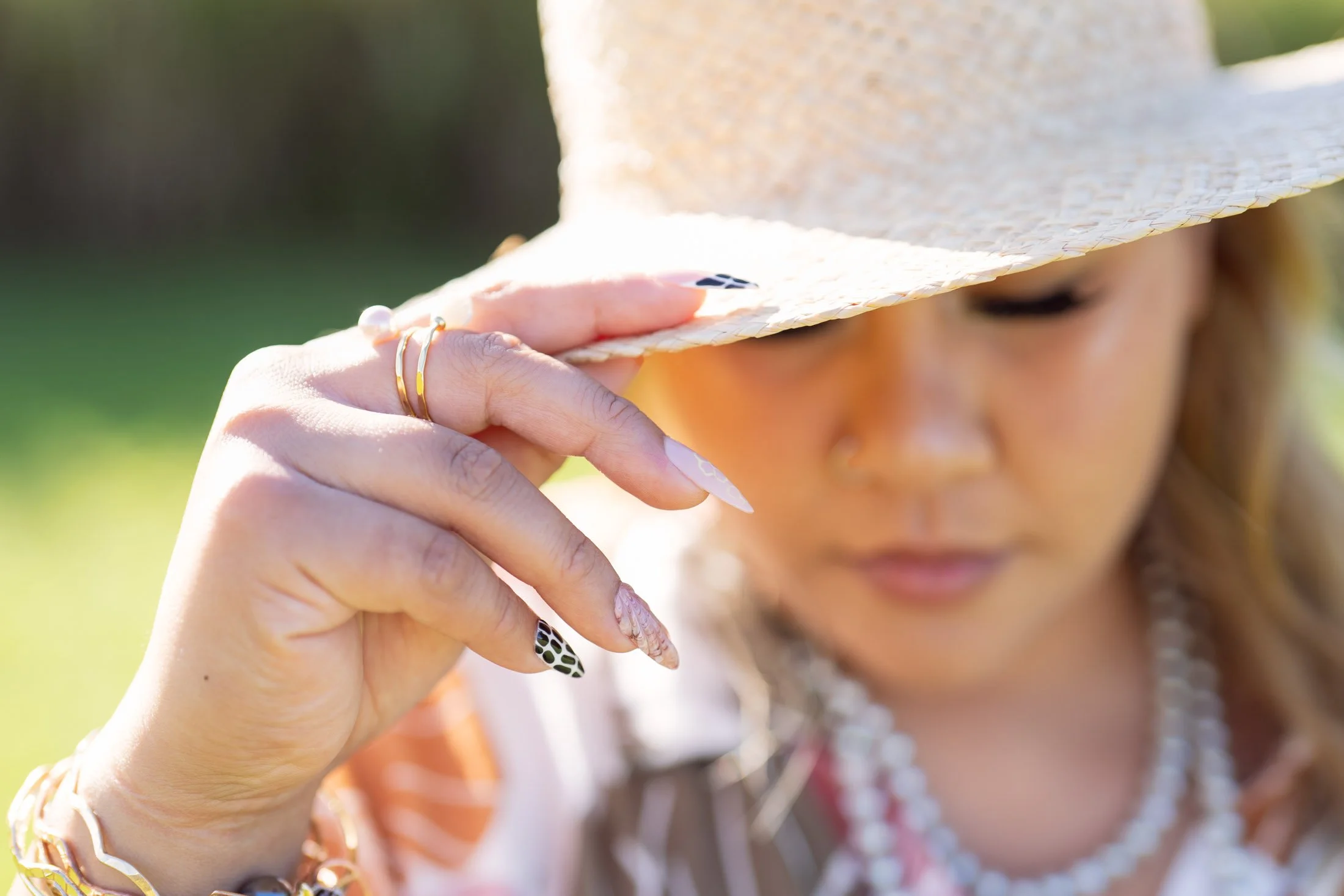 Woman wearing a straw hat tilting it down, her face slightly blurred, with detailed nails and jewelry visible on her hand for her maui personal branding photographer.