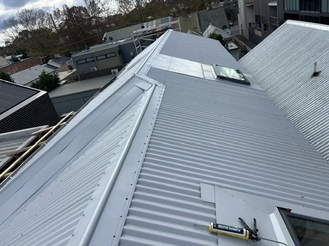 View of a metal roof with skylights and a solar panel on top, seen from above in a residential neighborhood.